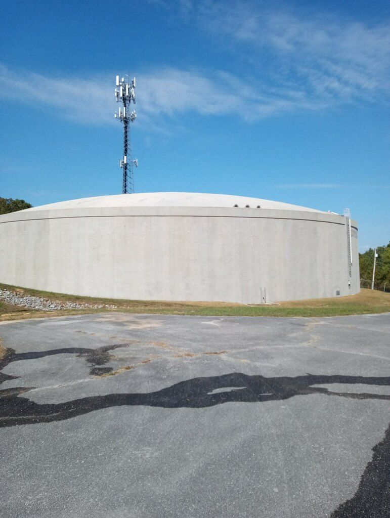 A tall, concrete water tower with a cell tower on top sits under a blue sky.