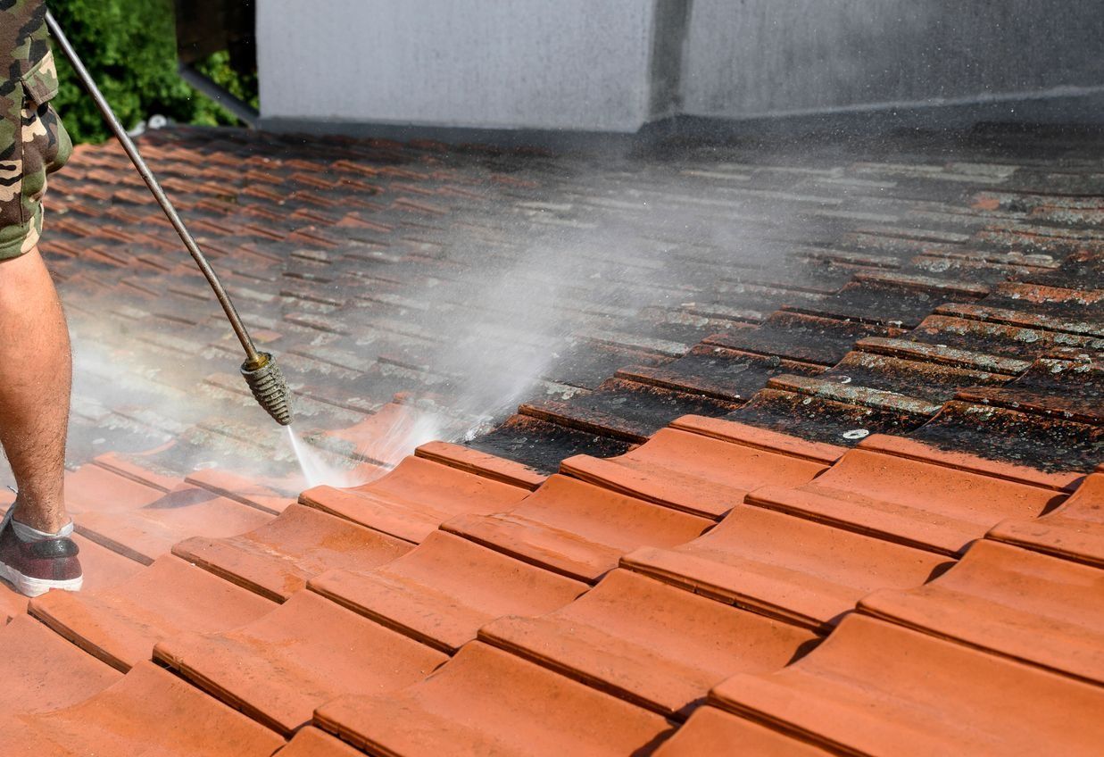 Pressure washing terracotta roof tiles with a spray wand, rinsing dirt from a sloped roof