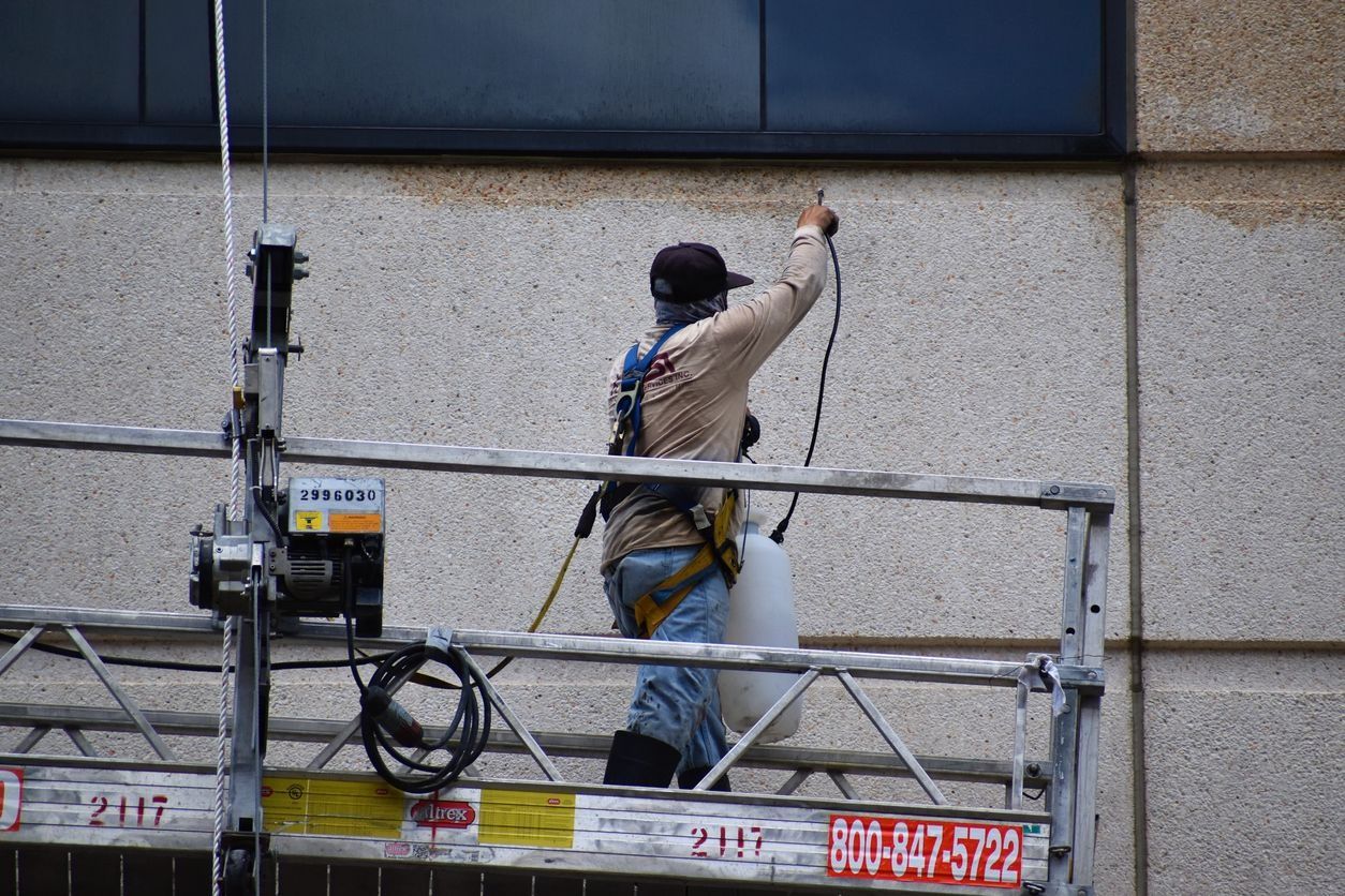 Worker on scaffolding cleaning a building exterior with a hose and safety gear