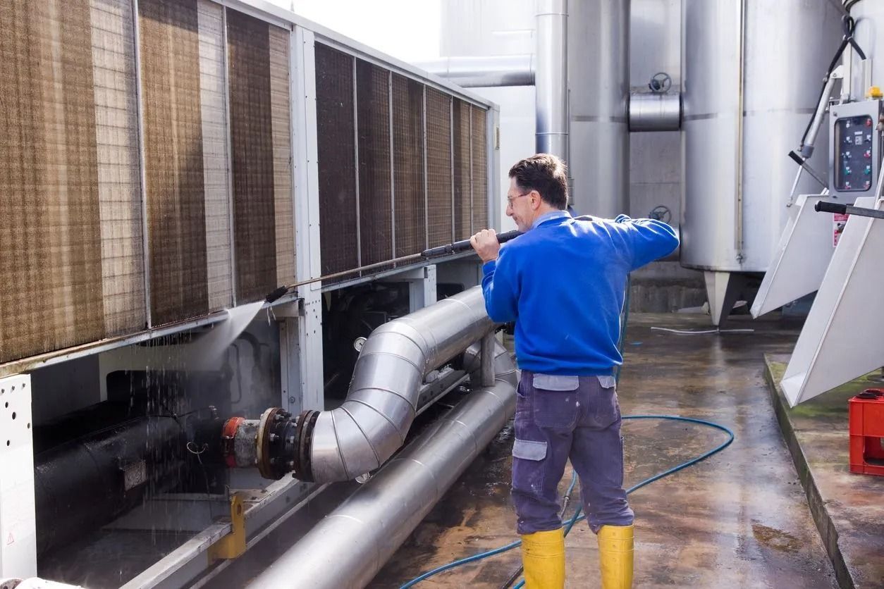 Worker in blue jacket inspecting industrial equipment with large metal pipes in a factory.