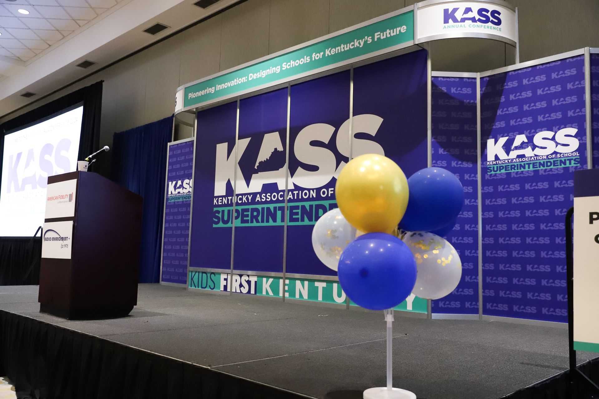 A podium with balloons in front of a sign that says kass