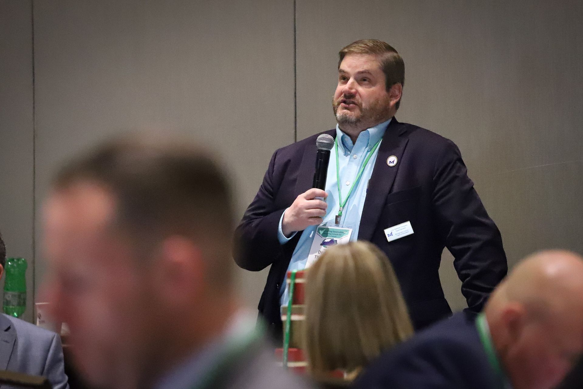 A man in a suit is speaking into a microphone at a conference.