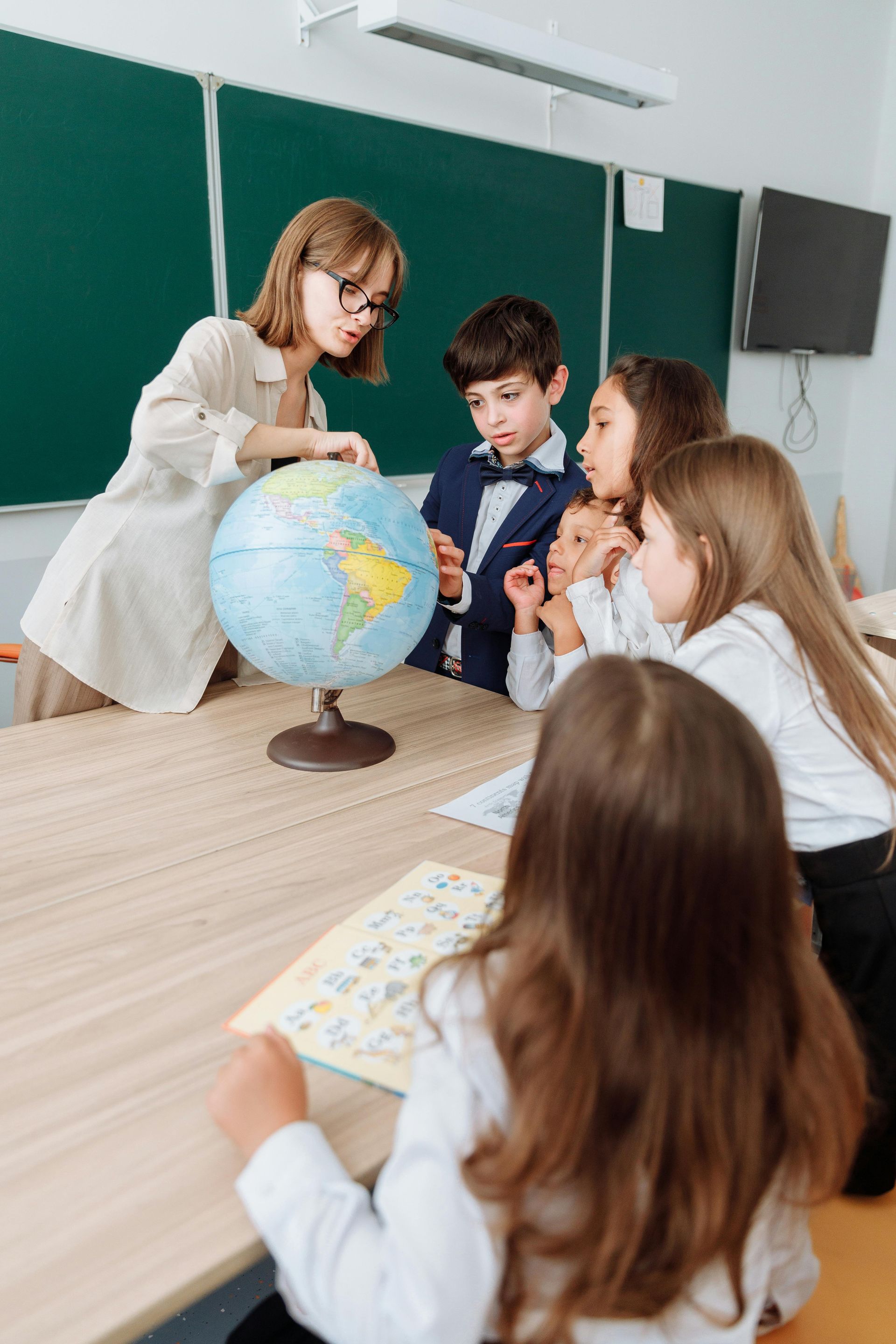 A group of children are sitting around a table looking at a globe.
