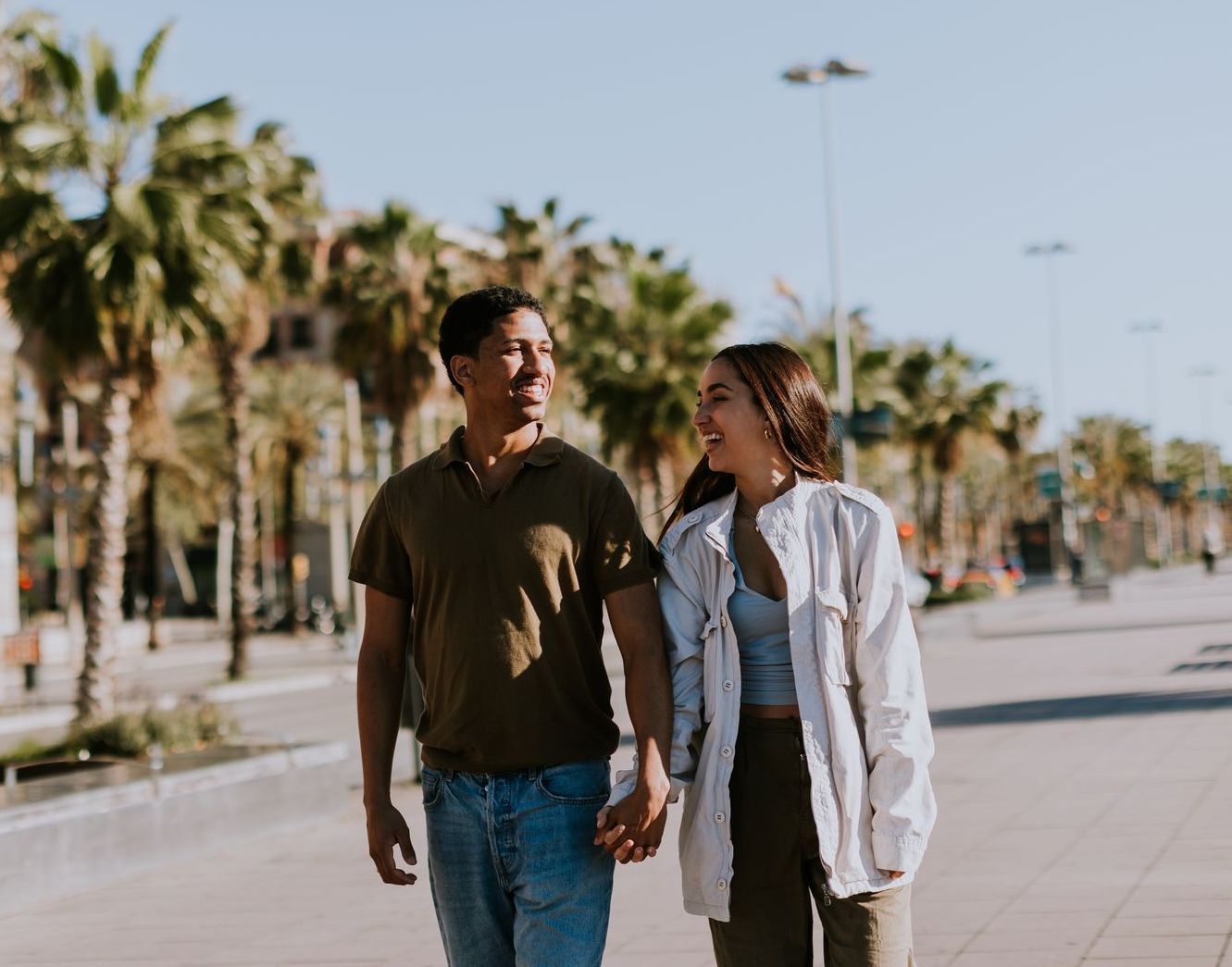 A man and a woman are walking down a sidewalk holding hands.