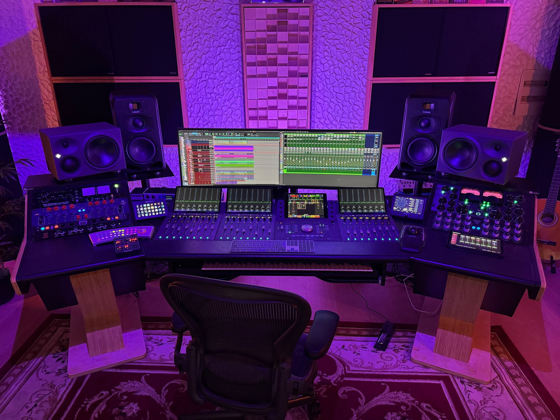 Recording studio with mixing console, monitors, and computer screens illuminated by purple light.
