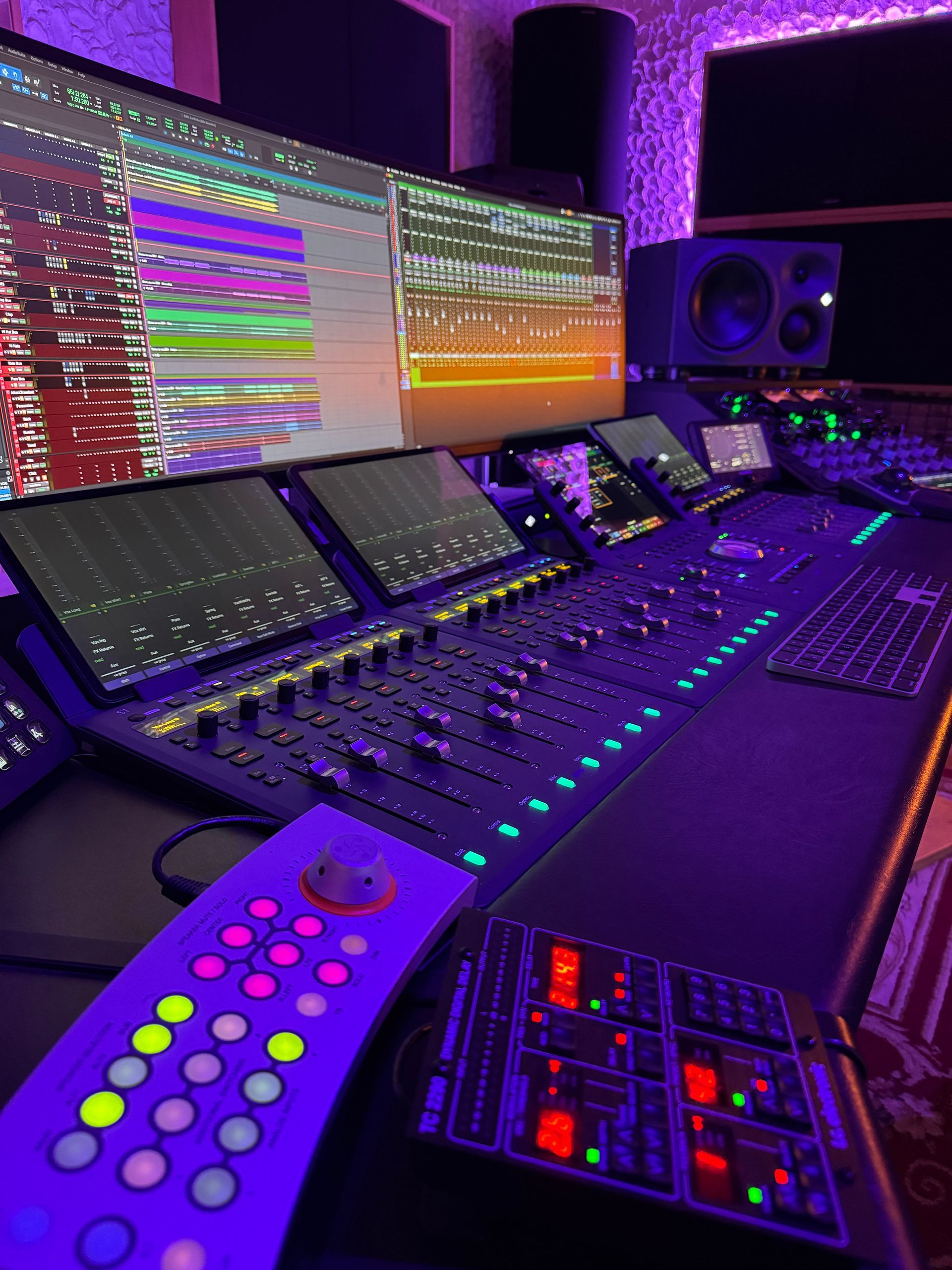 Recording studio control board with multiple screens, lit with purple hues, displaying audio waveforms.