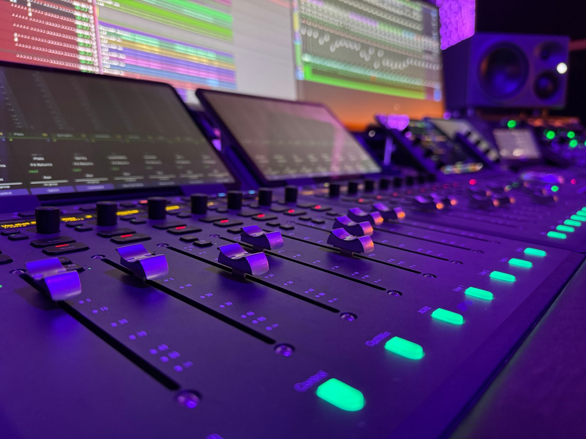 Close-up of a sound mixing console with multiple faders and glowing buttons in a recording studio.