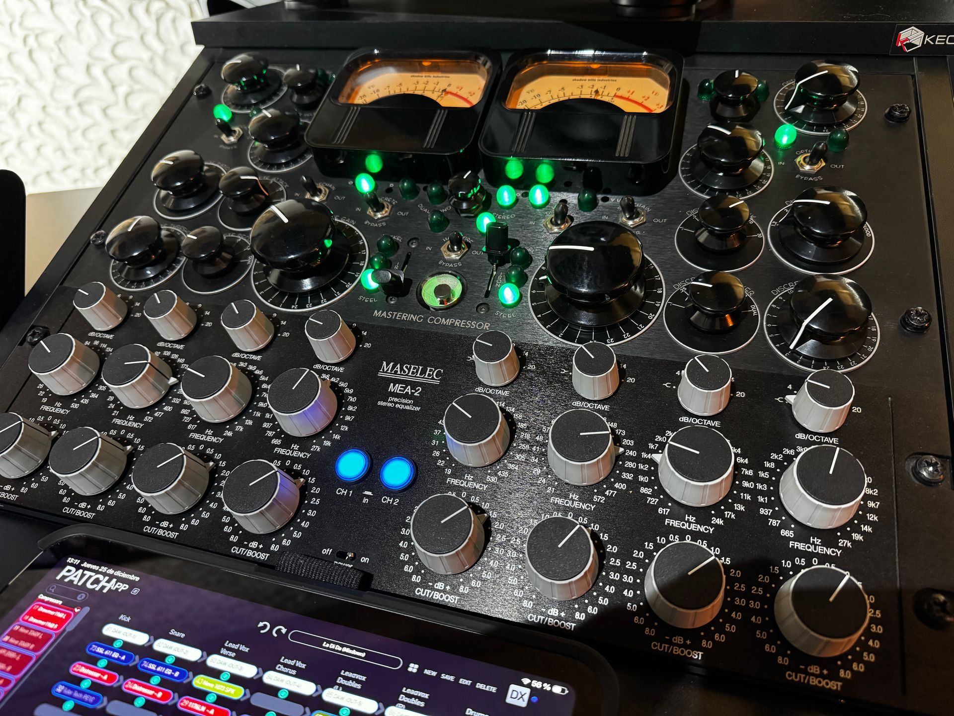 Black audio equipment with knobs and meters lit in green; a tablet displaying colorful visuals is in the foreground.