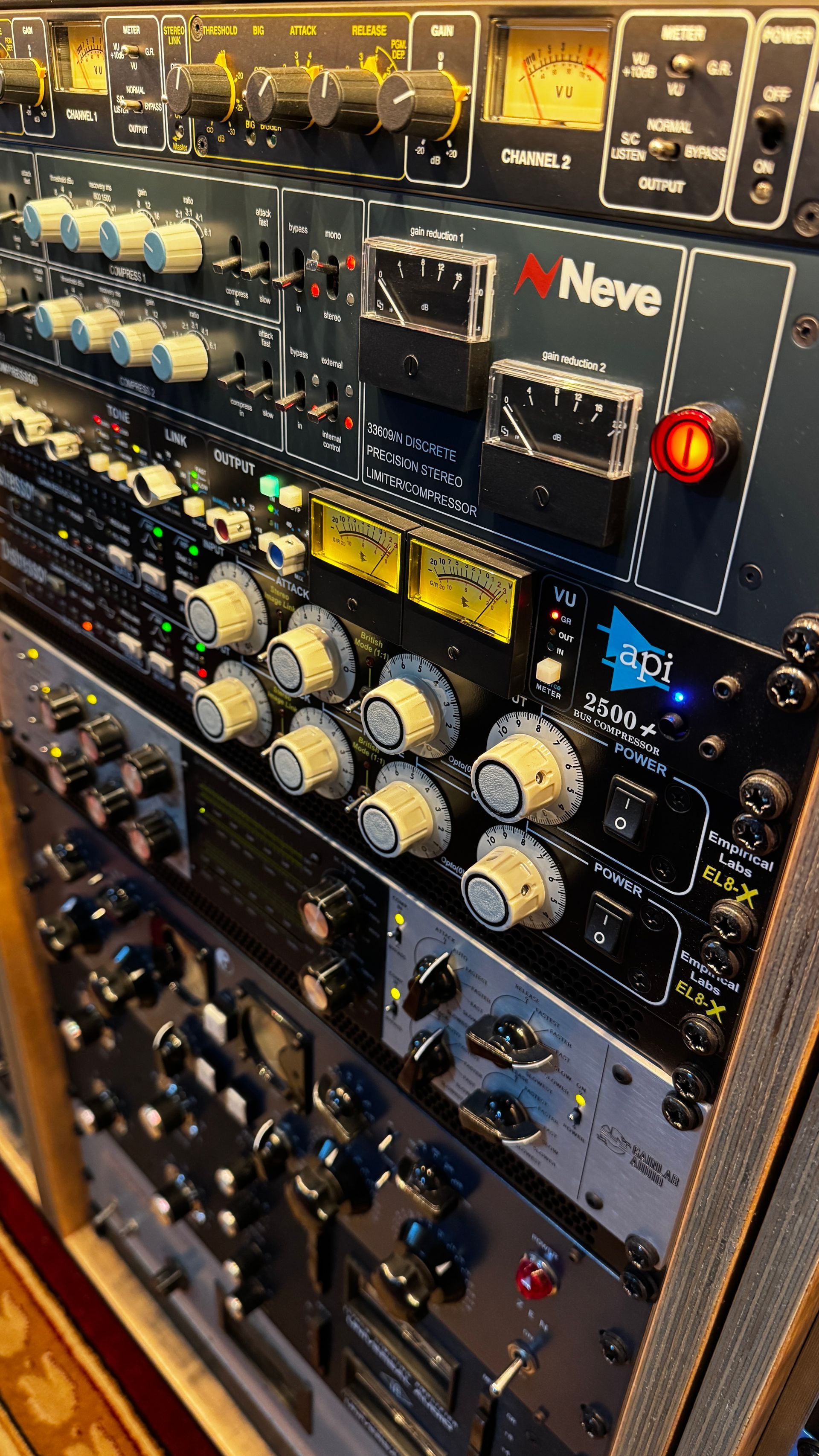 Close-up of a rack of audio equipment with knobs, buttons, and meters in a studio.