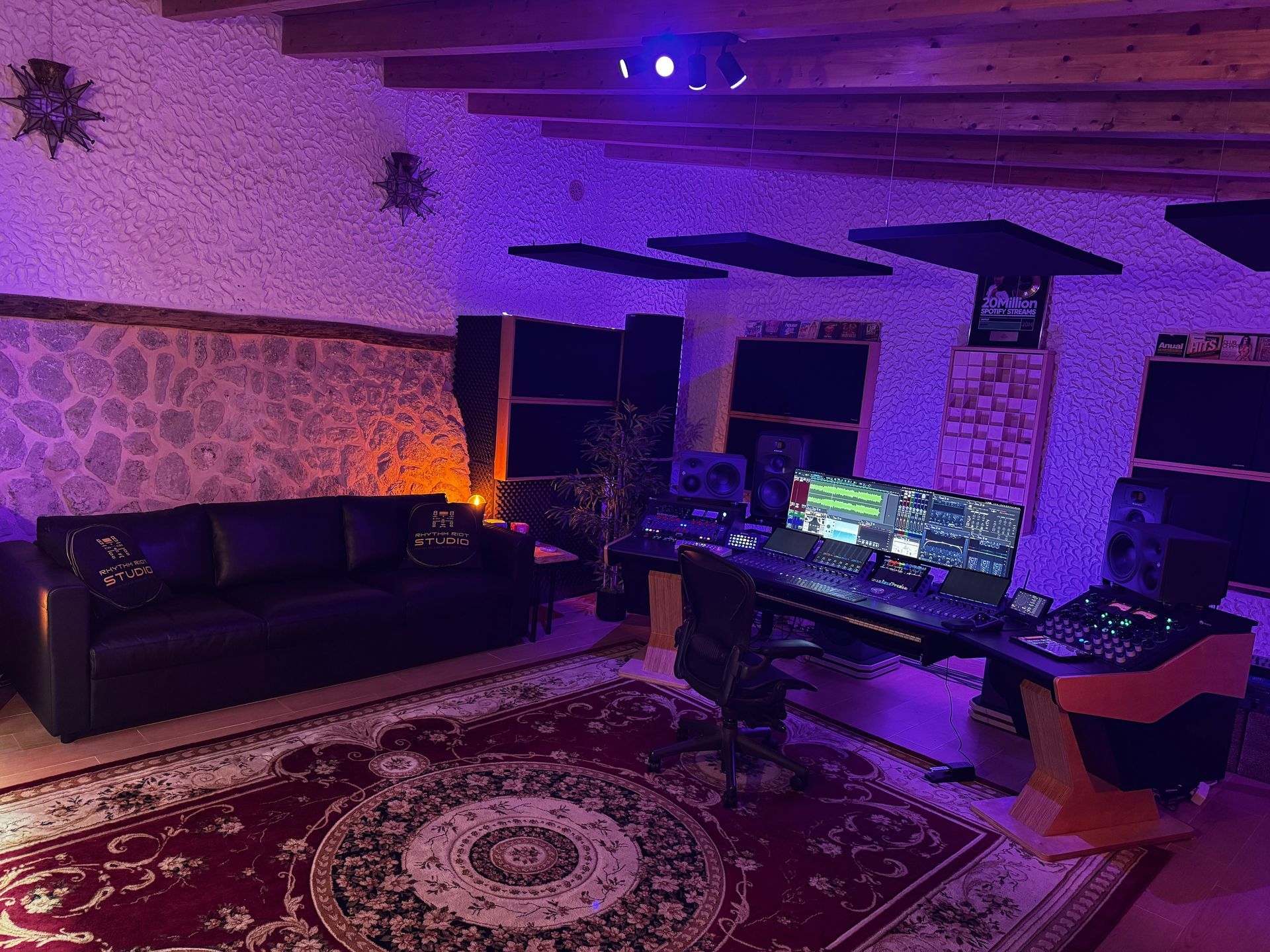 Recording studio with a couch, Persian rug, and mixing console, illuminated with purple and orange lights.