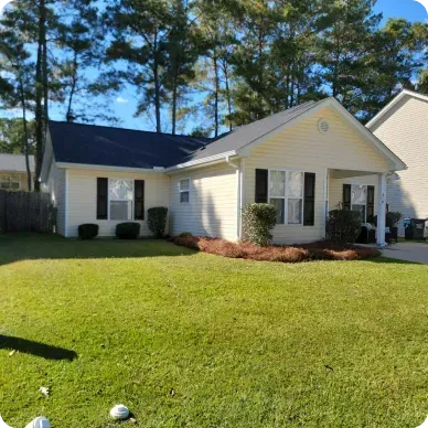 Yellow house with black shutters, black roof, and green lawn on a sunny day.