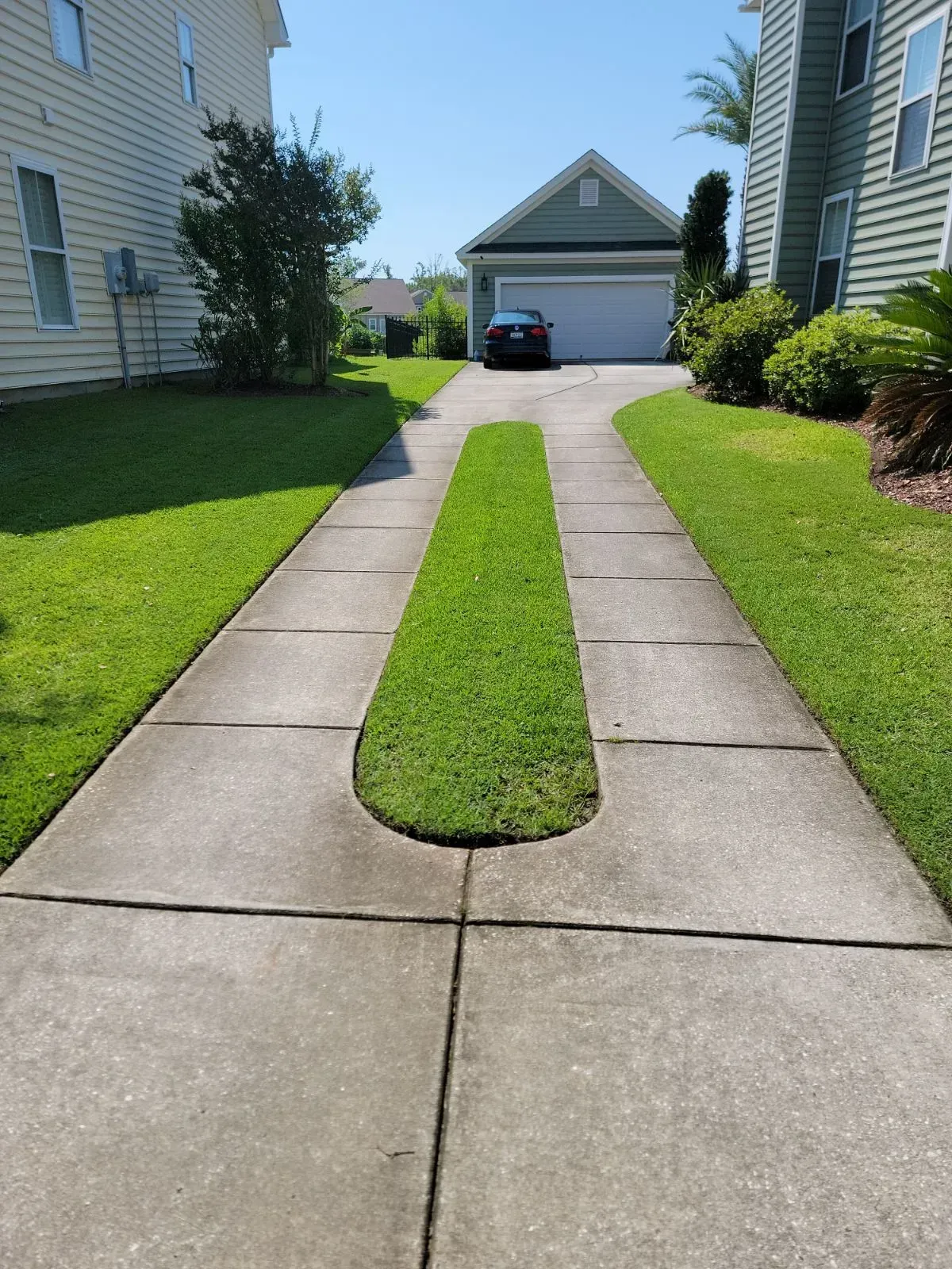 Driveway with grass median leading to a garage; a car is parked in the driveway.