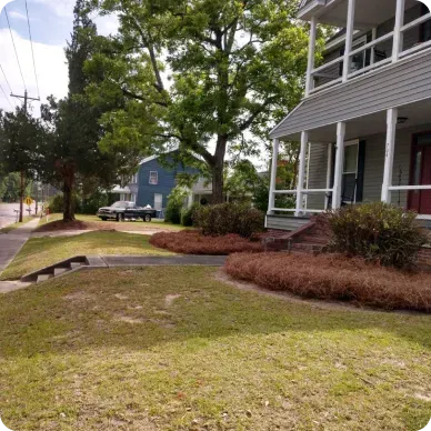 Lawn and house with porch; shrubs and trees surround the yard.
