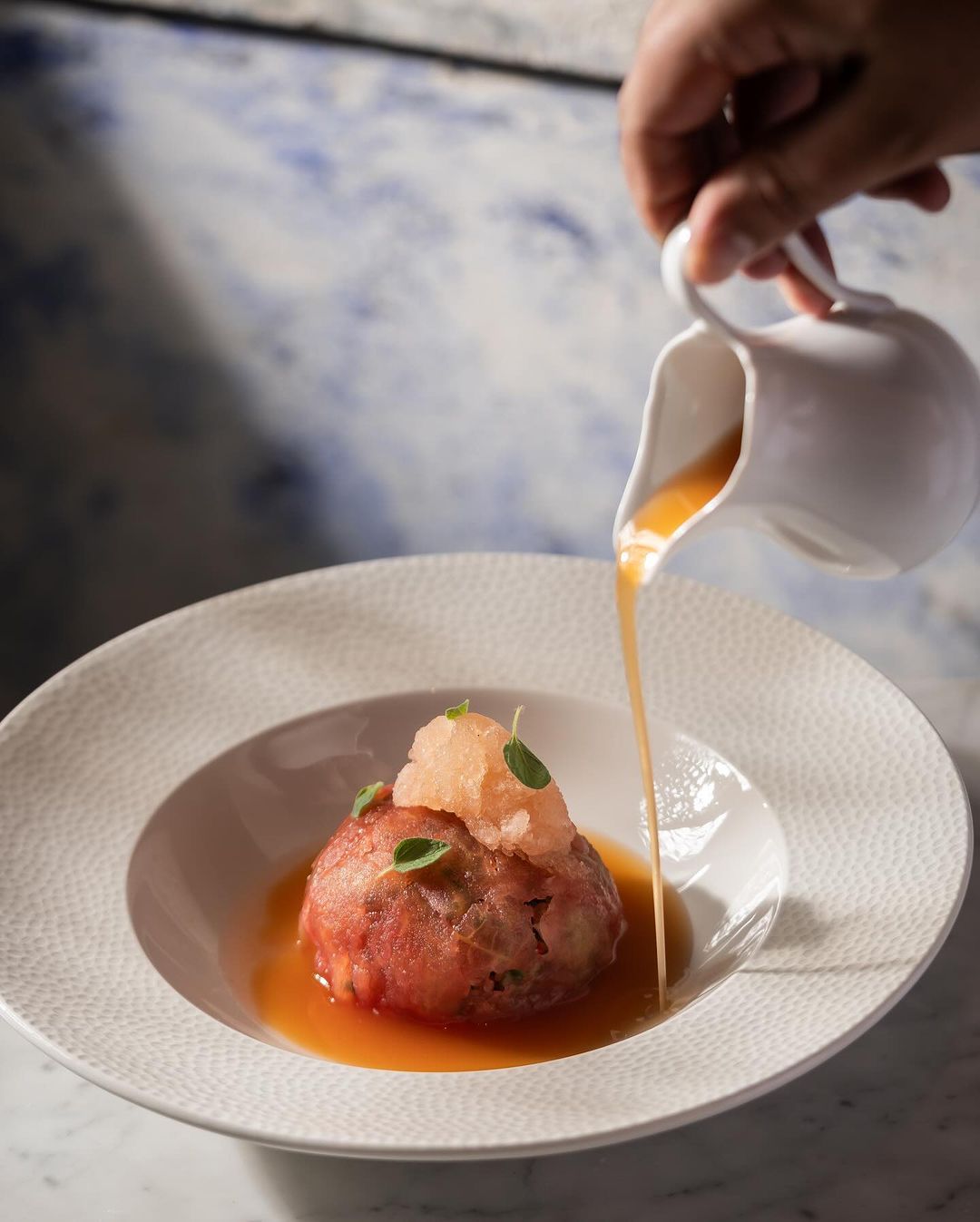 A person pouring sauce into a bowl of food