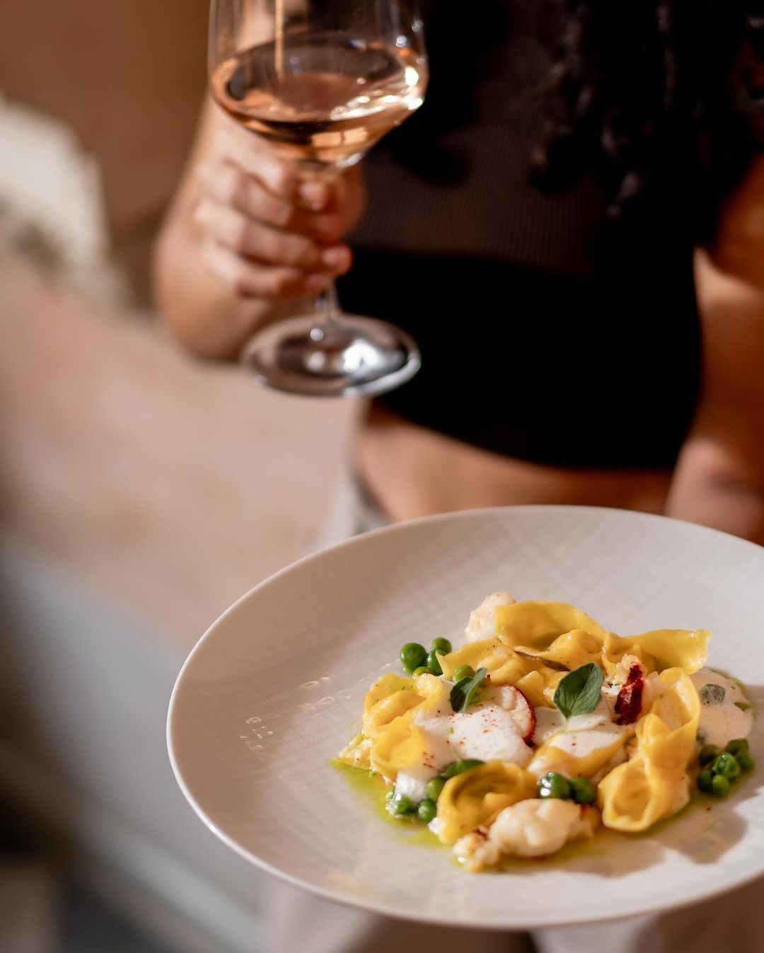 A woman is holding a glass of wine and a plate of food.