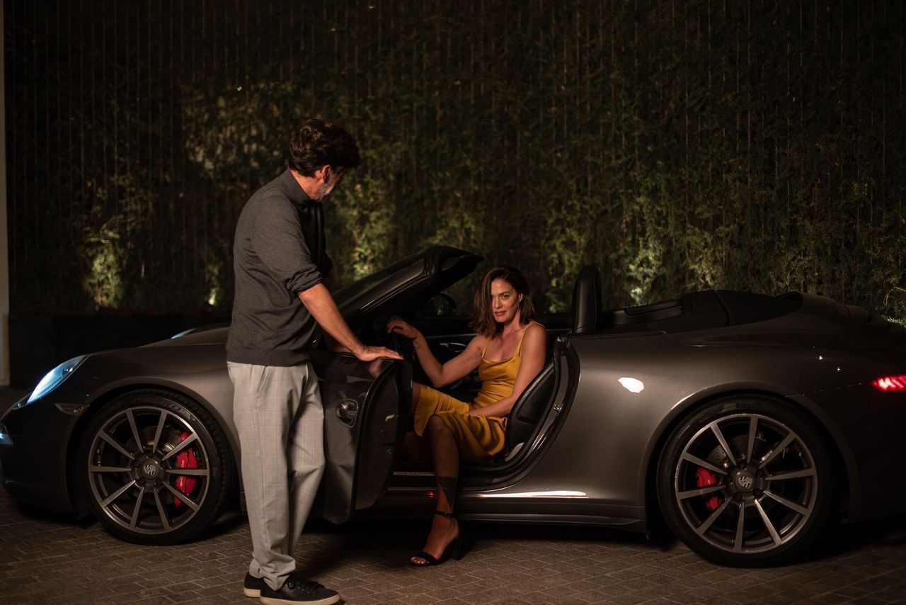 A man is helping a woman get out of a sports car.