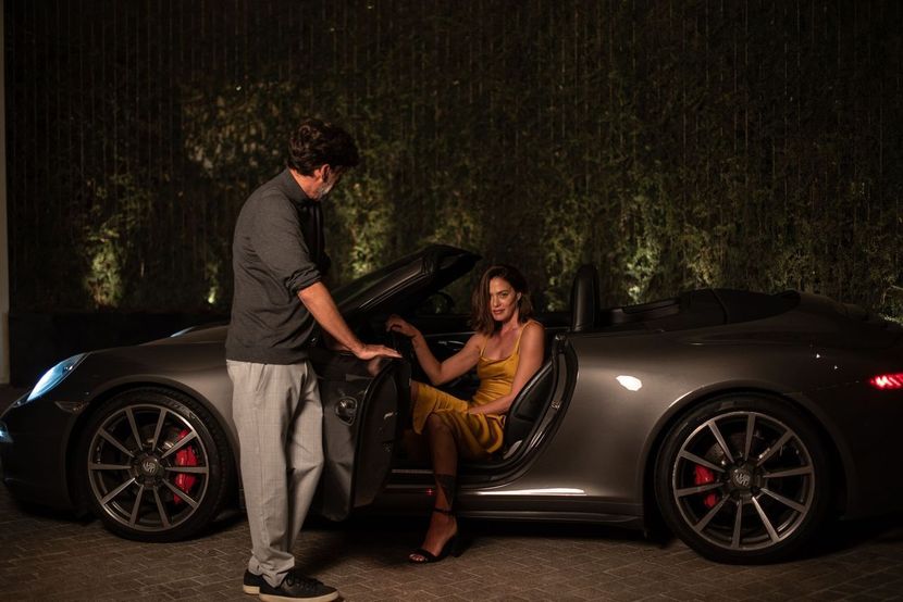 A man is helping a woman get out of a sports car.