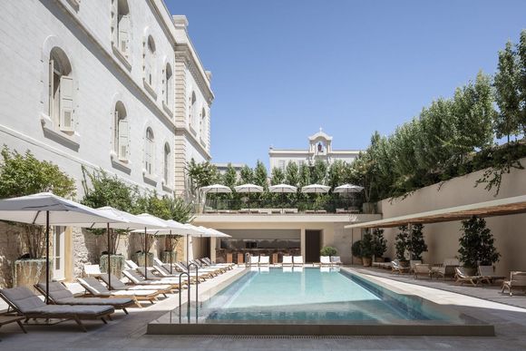 A large swimming pool surrounded by chairs and umbrellas in front of a building.