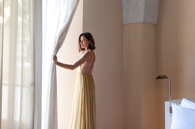 A woman in a long dress is standing in front of a window.