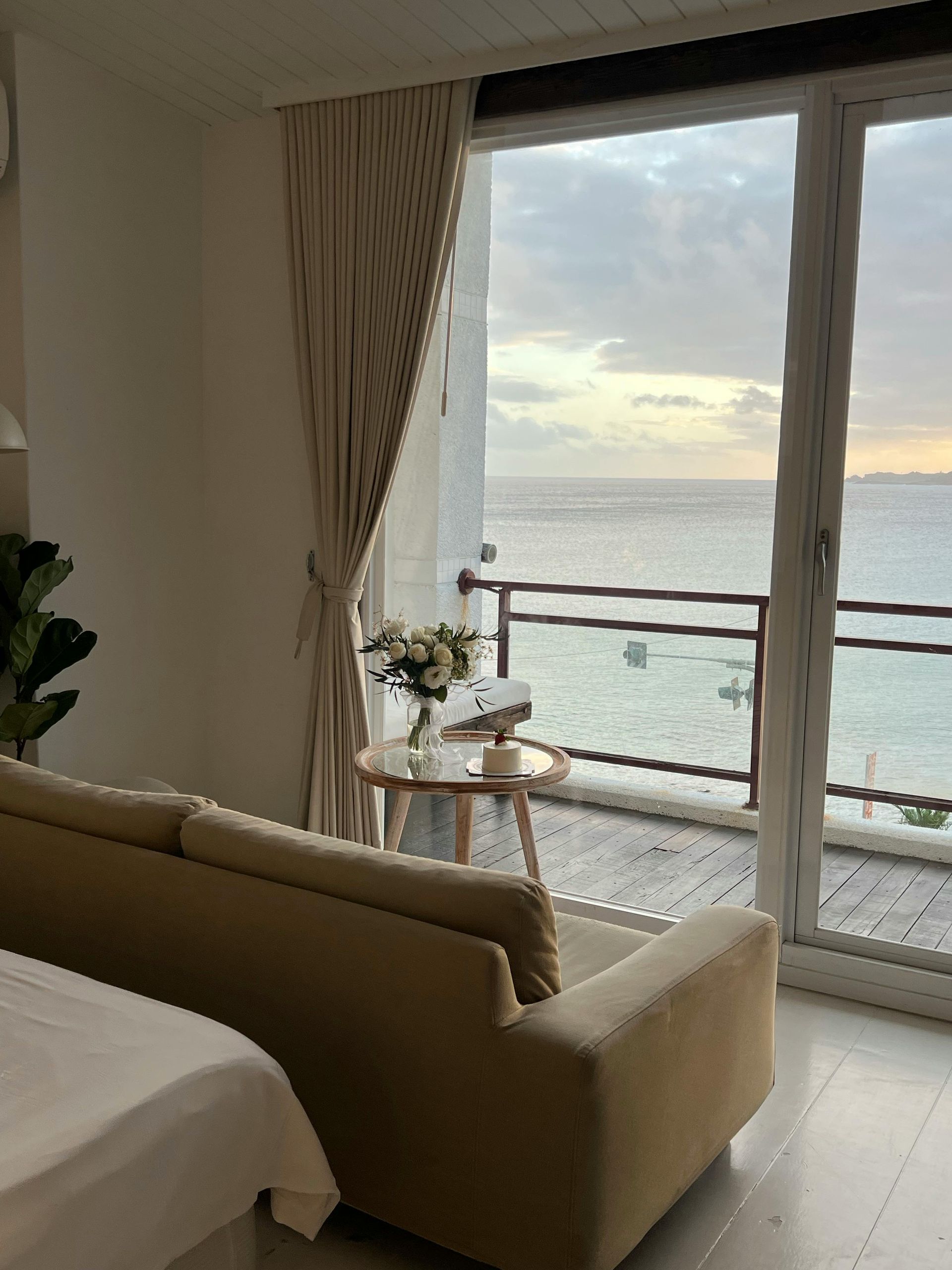 Room with a couch, table, and flowers overlooking the ocean through a sliding glass door.