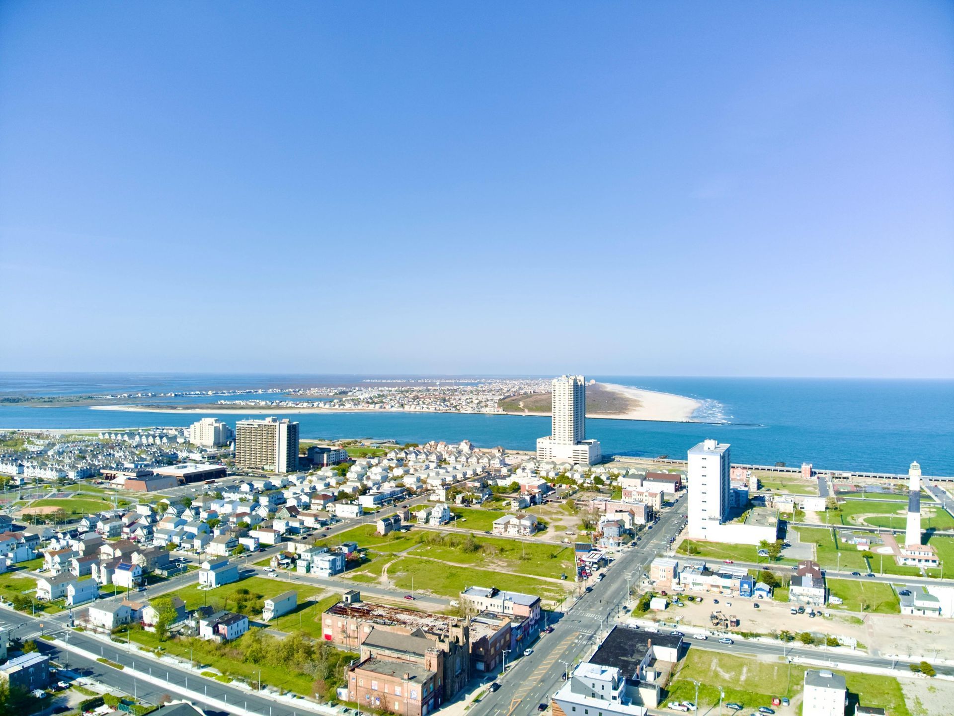 Coastal city aerial view with buildings, streets, and ocean under a blue sky.
