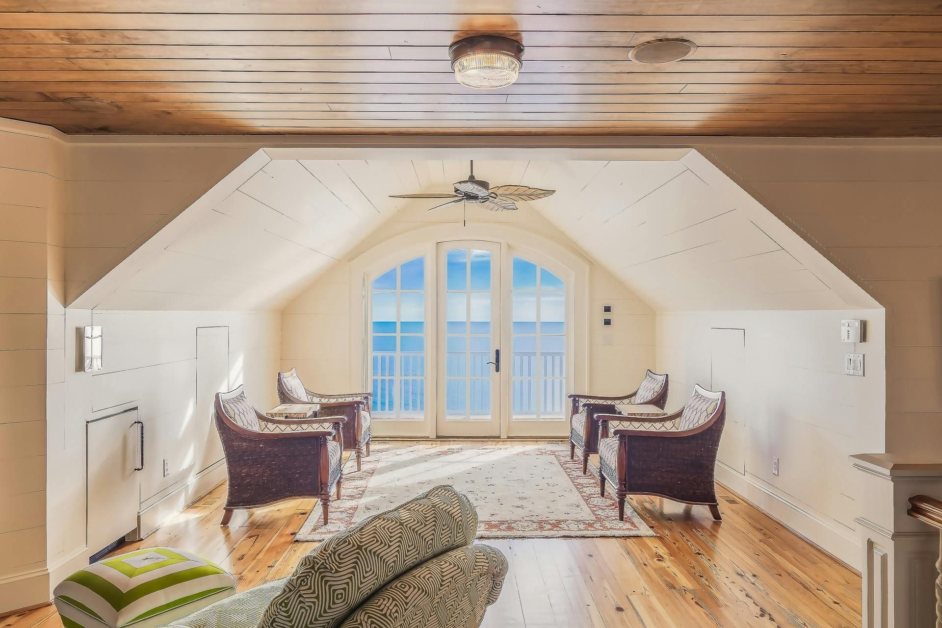Sunlit attic room with arched doors, wicker chairs, and wood ceiling.