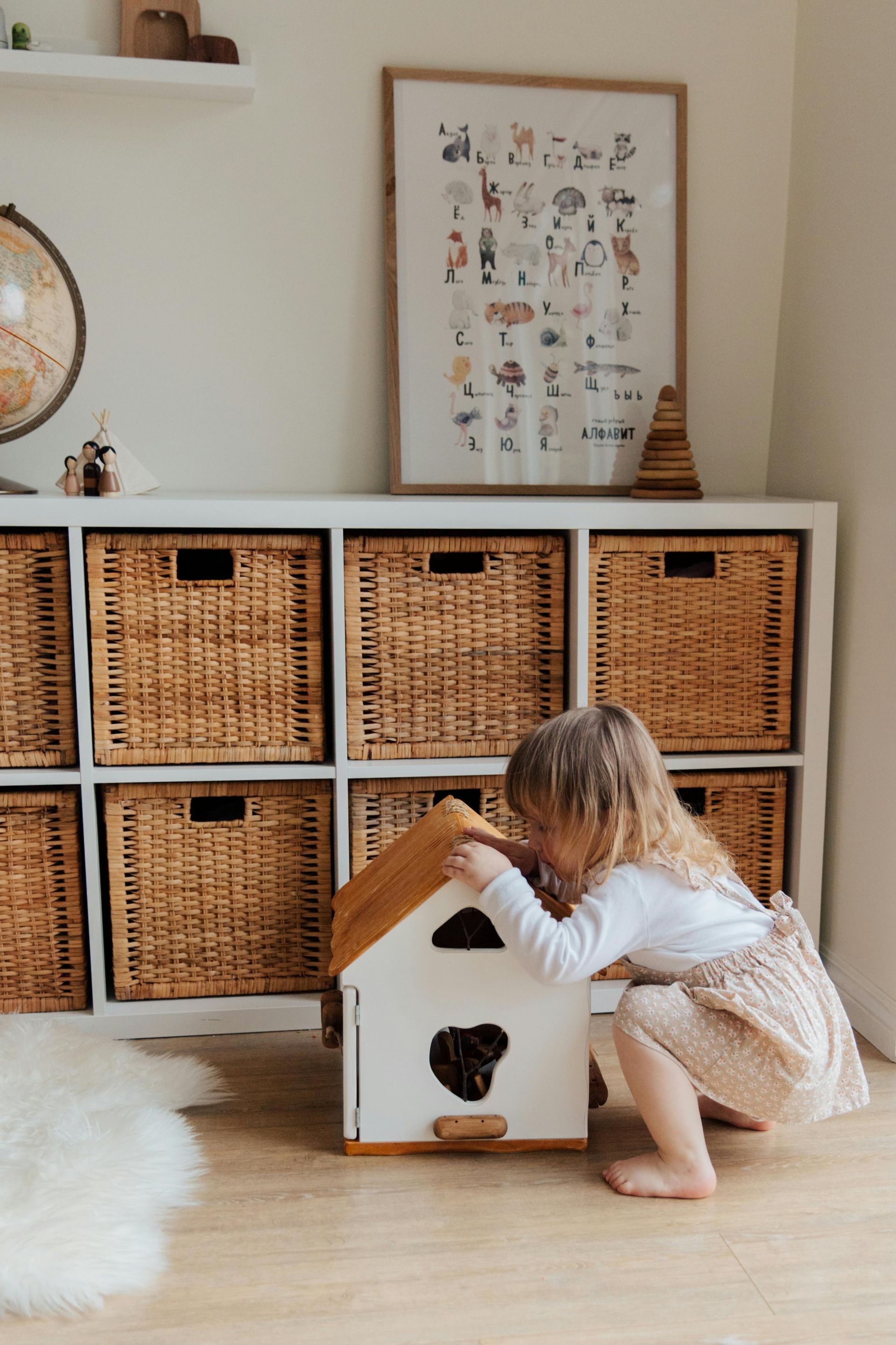 Child playing with a wooden toy house in a playroom with storage baskets.