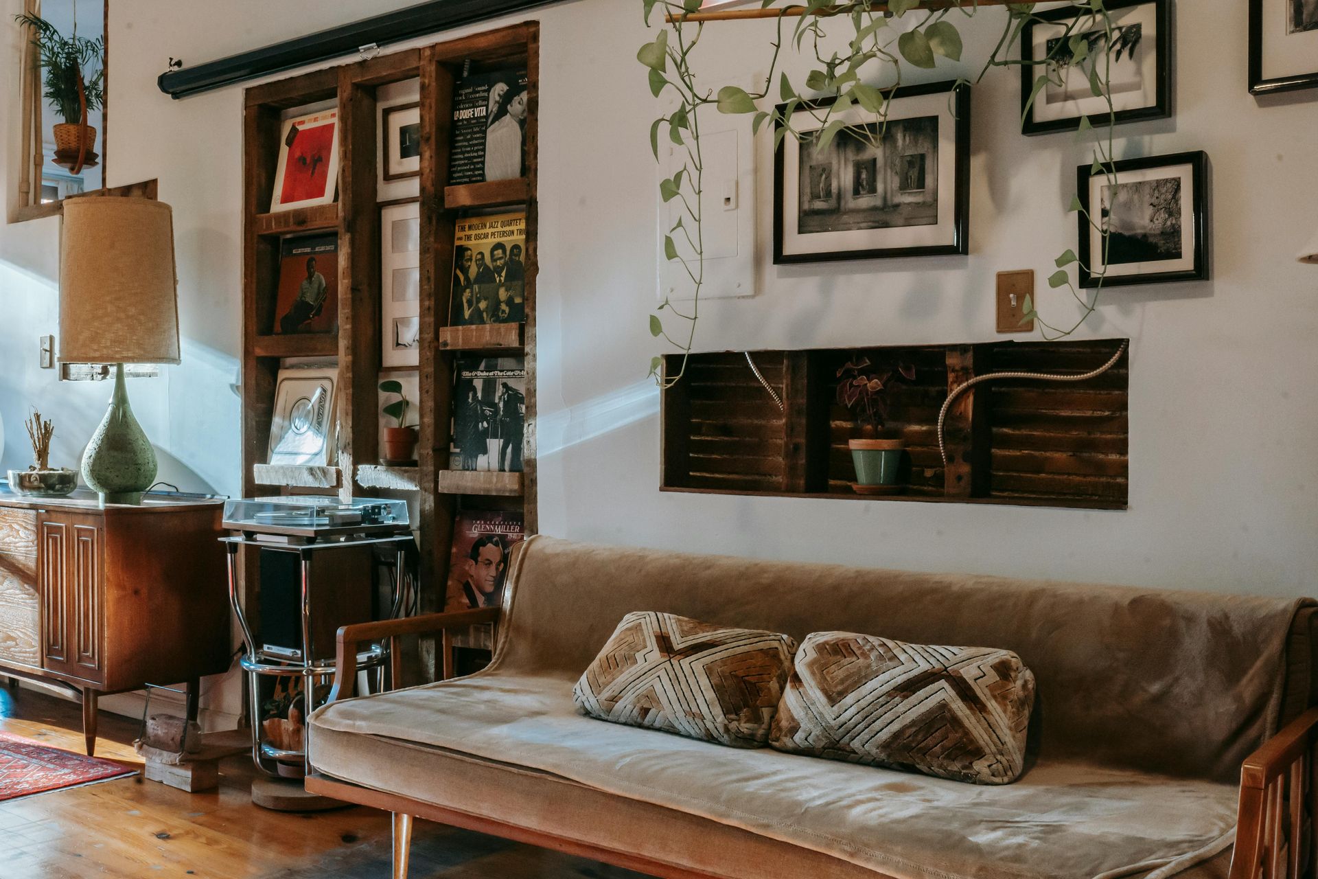 Cozy living room with a brown sofa, wooden bookshelf, and framed art on white walls.