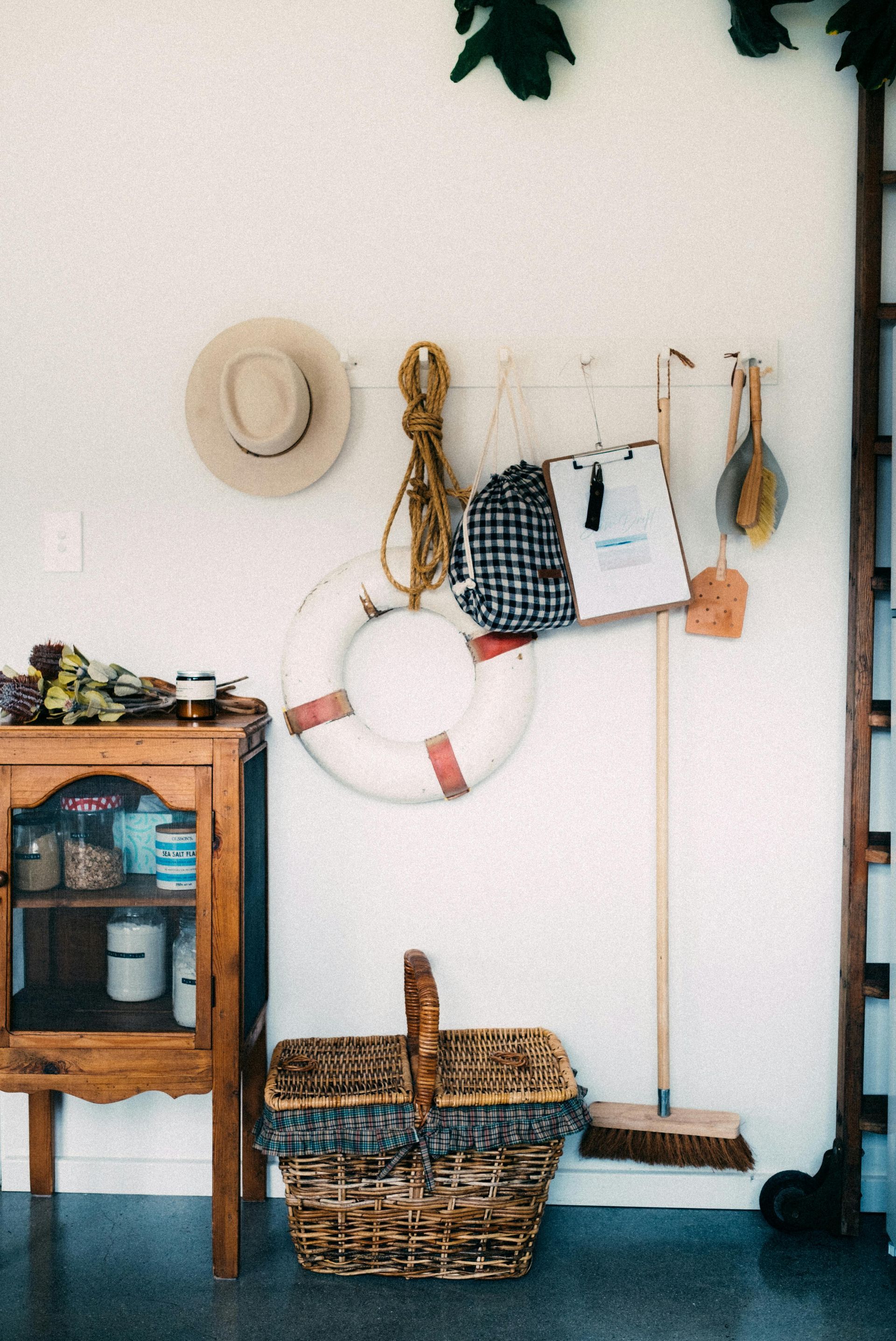 White wall with various items: hat, rope, life preserver, basket, broom, and cabinet.