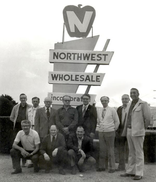 A group of men pose in front of a northwest wholesale sign