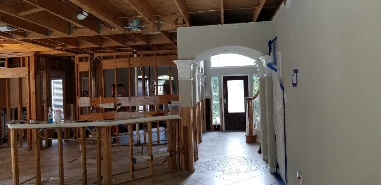 Interior of a house under renovation, with exposed framing, an archway, and a doorway at the end of a hallway.
