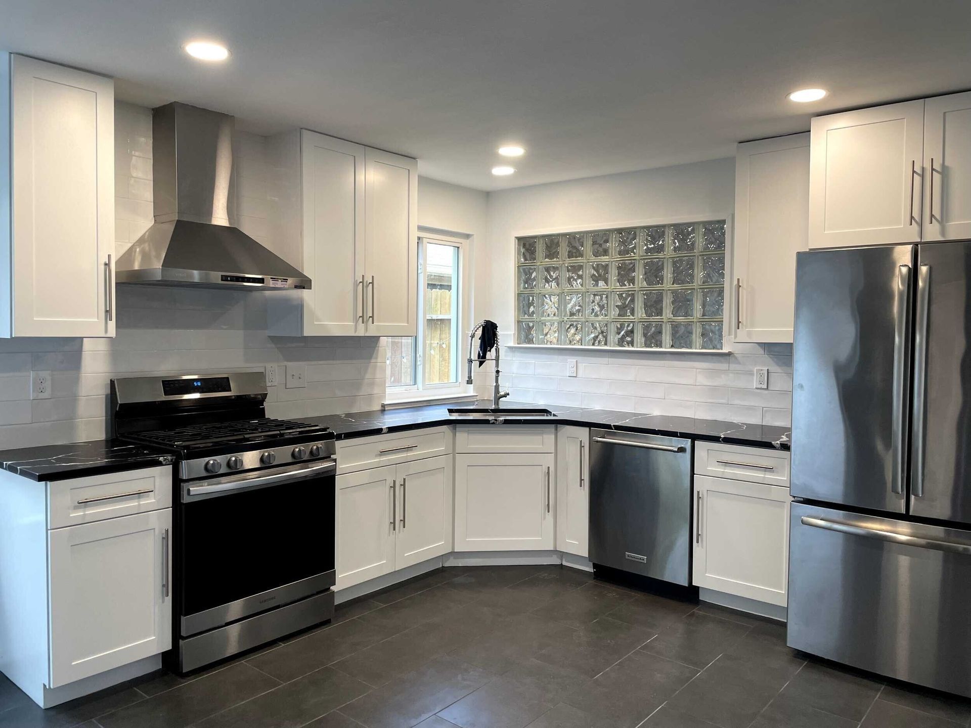White kitchen with stainless steel appliances, dark countertops, and tile backsplash.