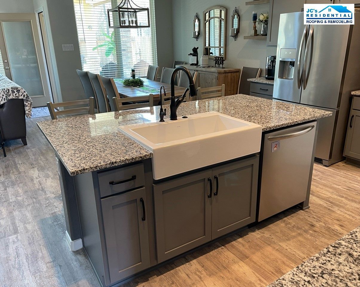 Kitchen island with a farmhouse sink, granite countertop, grey cabinets, and a dishwasher.