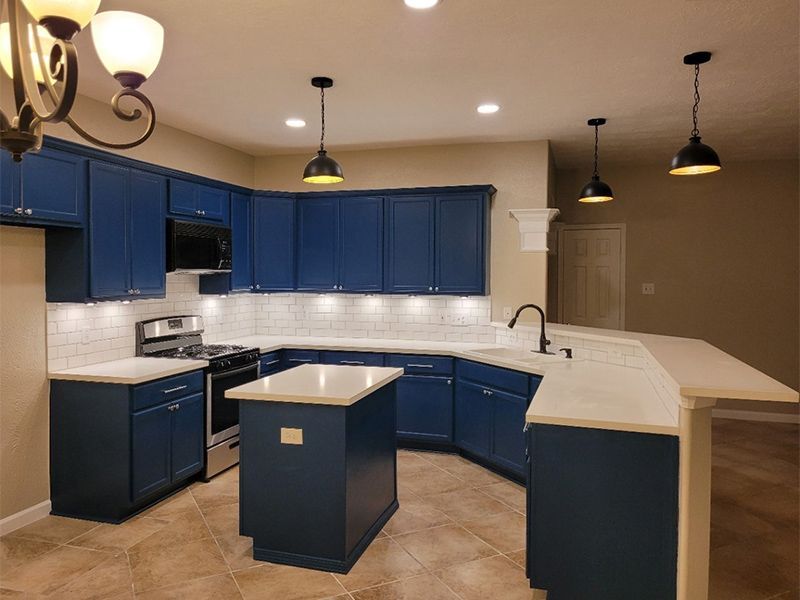 Blue kitchen cabinets with white countertops and pendant lights, kitchen island.