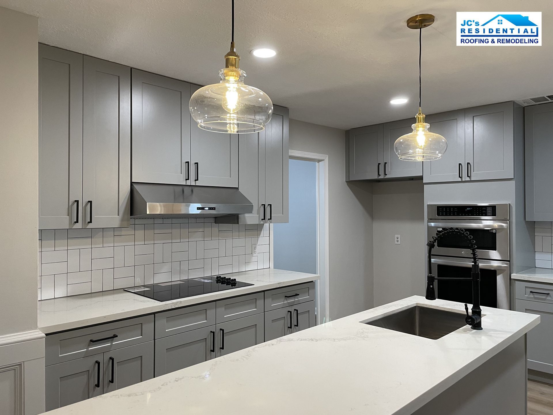 Modern kitchen with gray cabinets, white countertops, and hanging glass pendant lights.