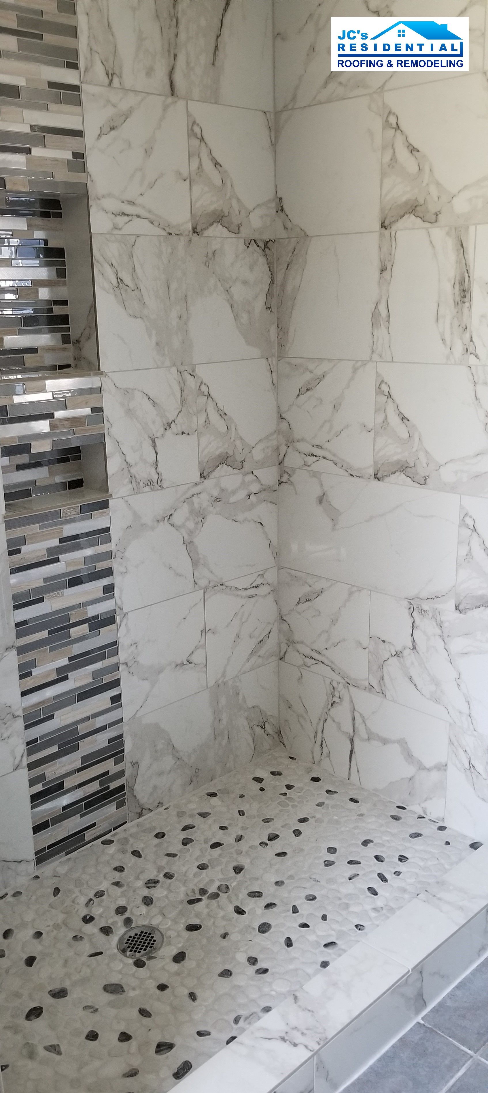 Shower with marble-look tile walls, a pebble-tiled floor, and a decorative tile wall.