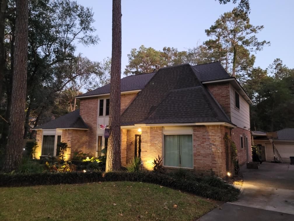Two-story brick house at dusk, with landscape lighting illuminating the front yard and driveway.