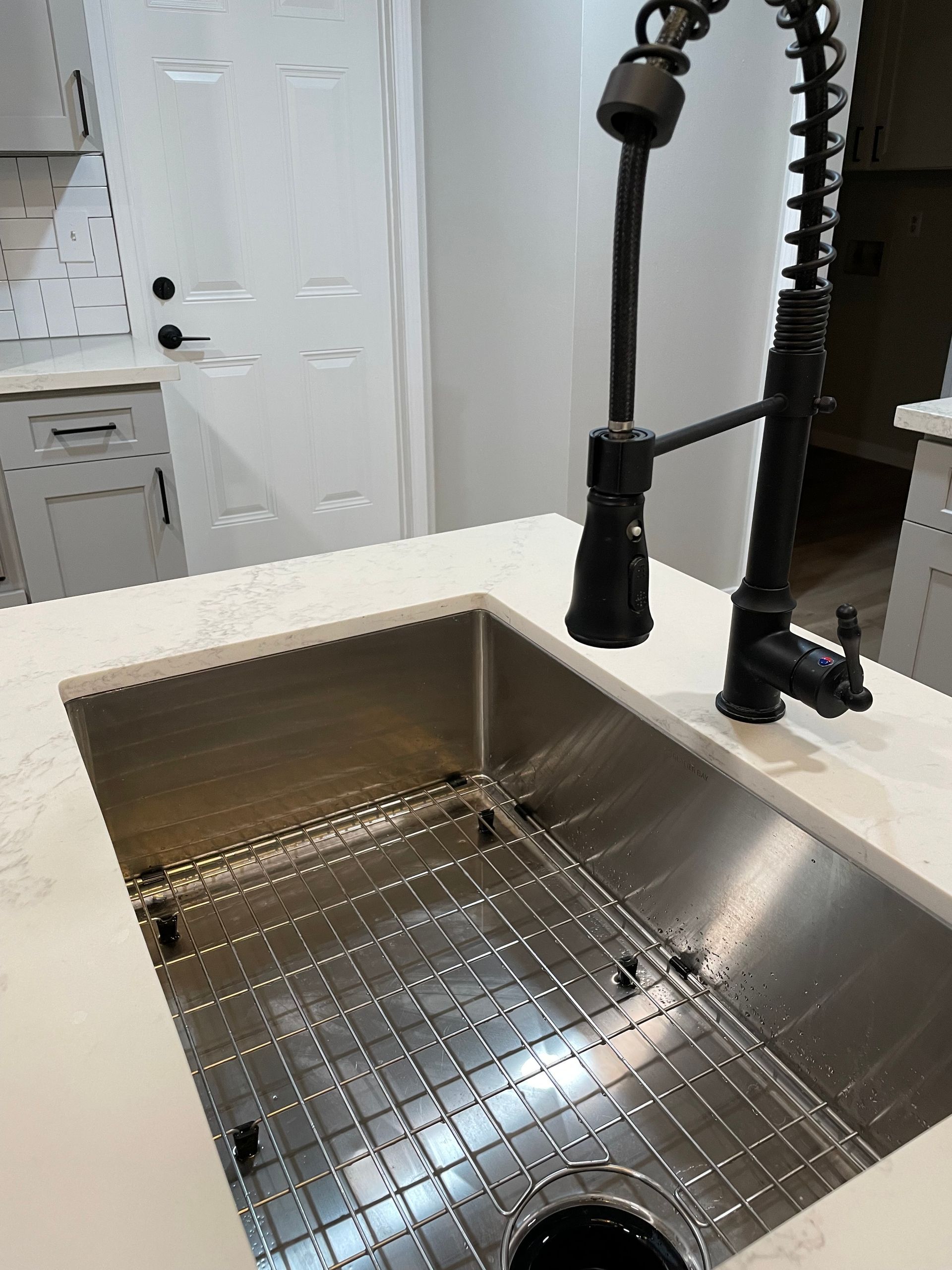 Stainless steel kitchen sink with black faucet on white countertop.
