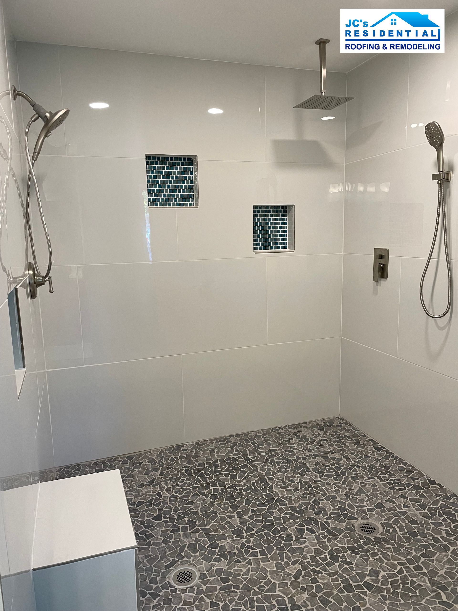 Modern walk-in shower with white tile walls, pebble floor, and multiple shower heads.