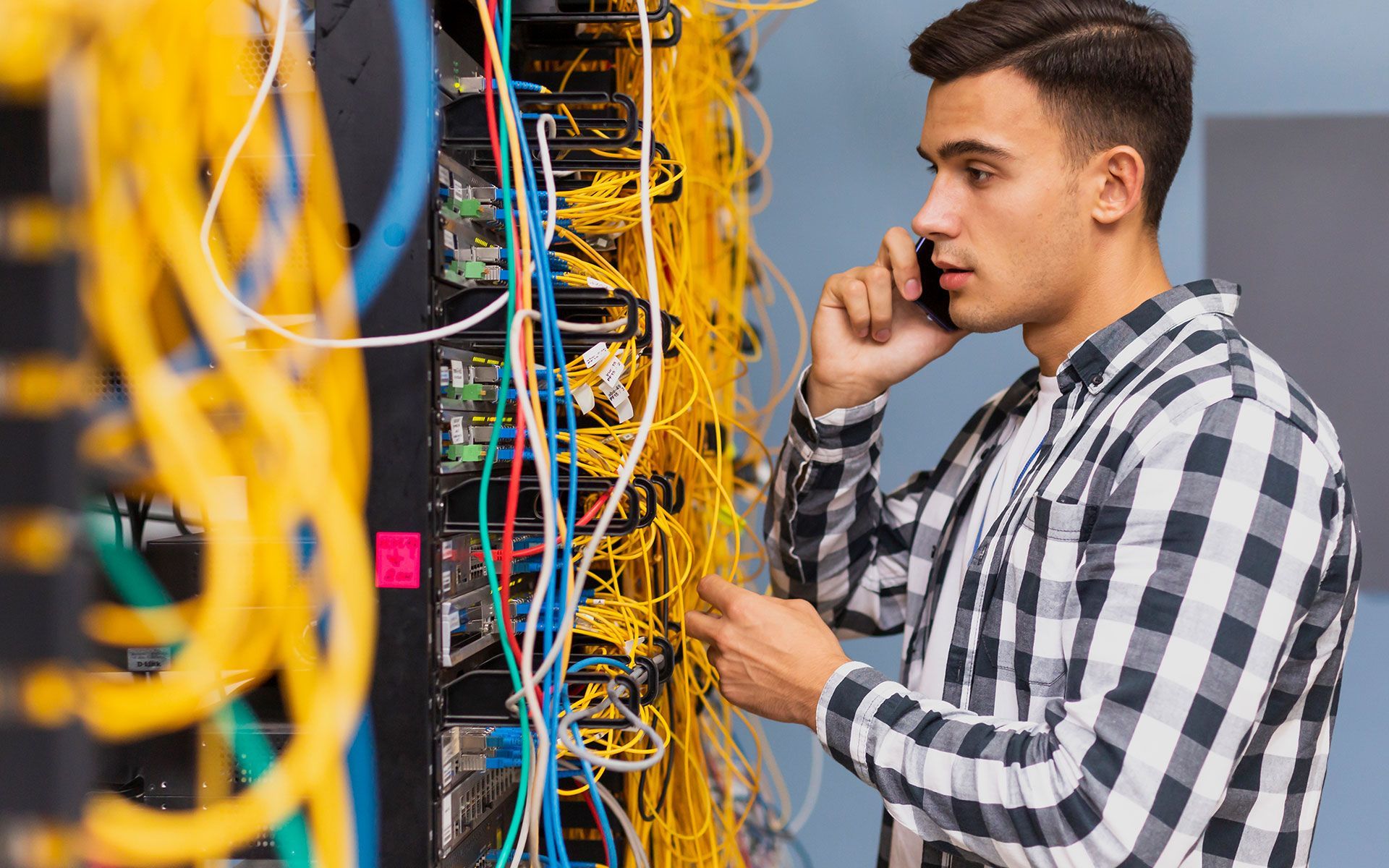 A man is talking on a cell phone while working on a server.