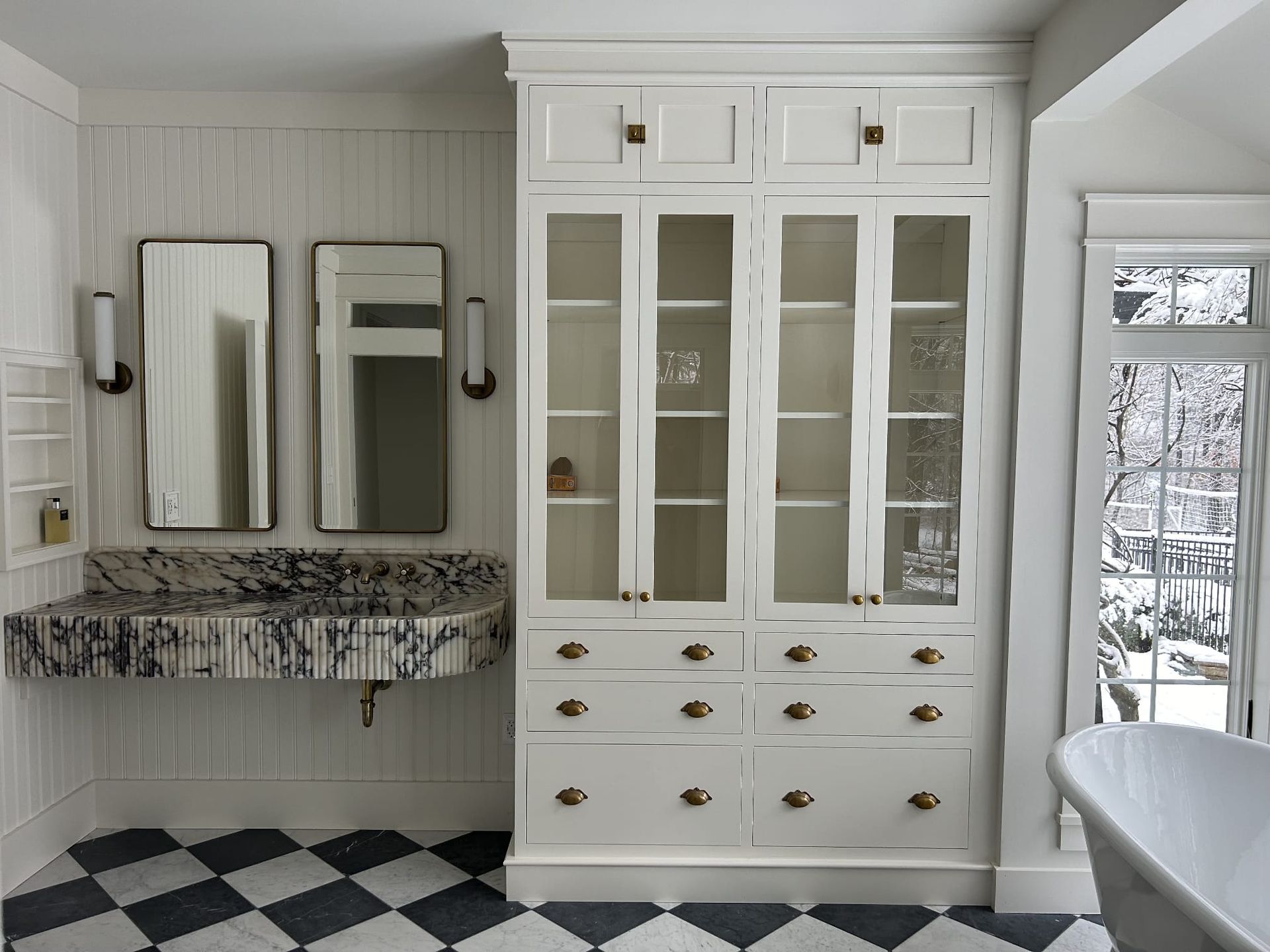 Bright bathroom with white vanity cabinet, mirrors, floral counter, and checkered black-and-white tile floor.