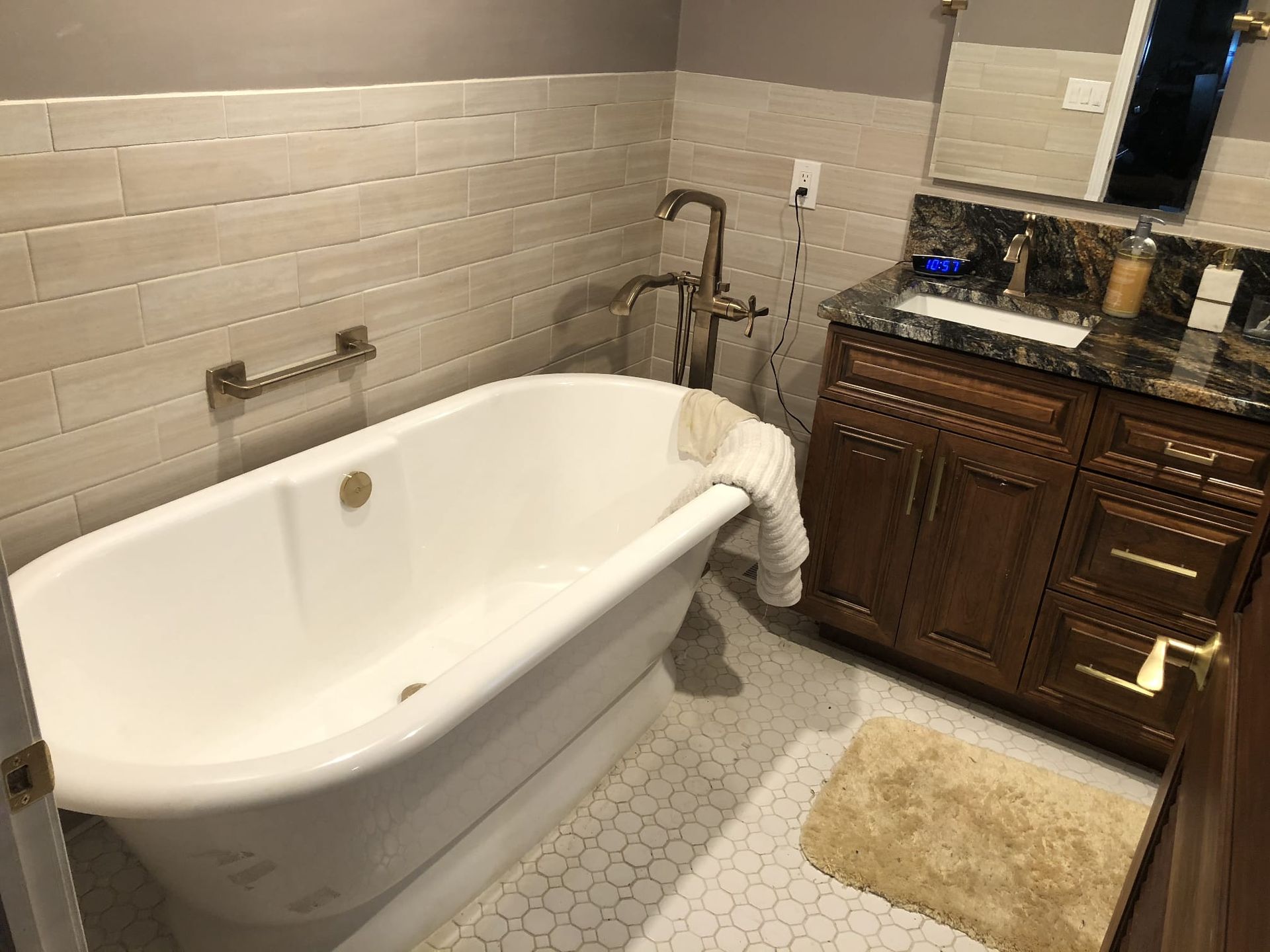 Bathroom with a white clawfoot tub, tiled walls, wooden vanity, and a beige bath mat.