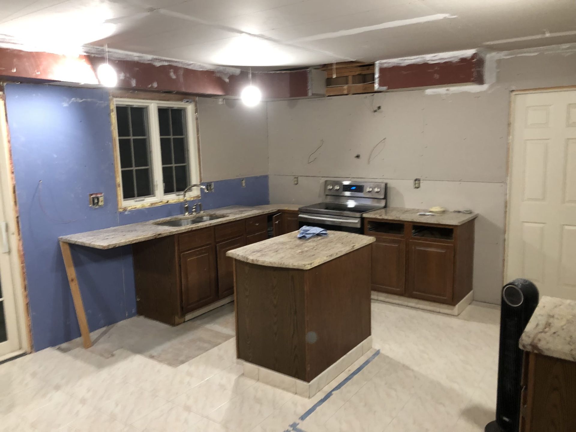 Partially renovated kitchen with cabinets, granite island, blue accent wall, and exposed ceiling wiring