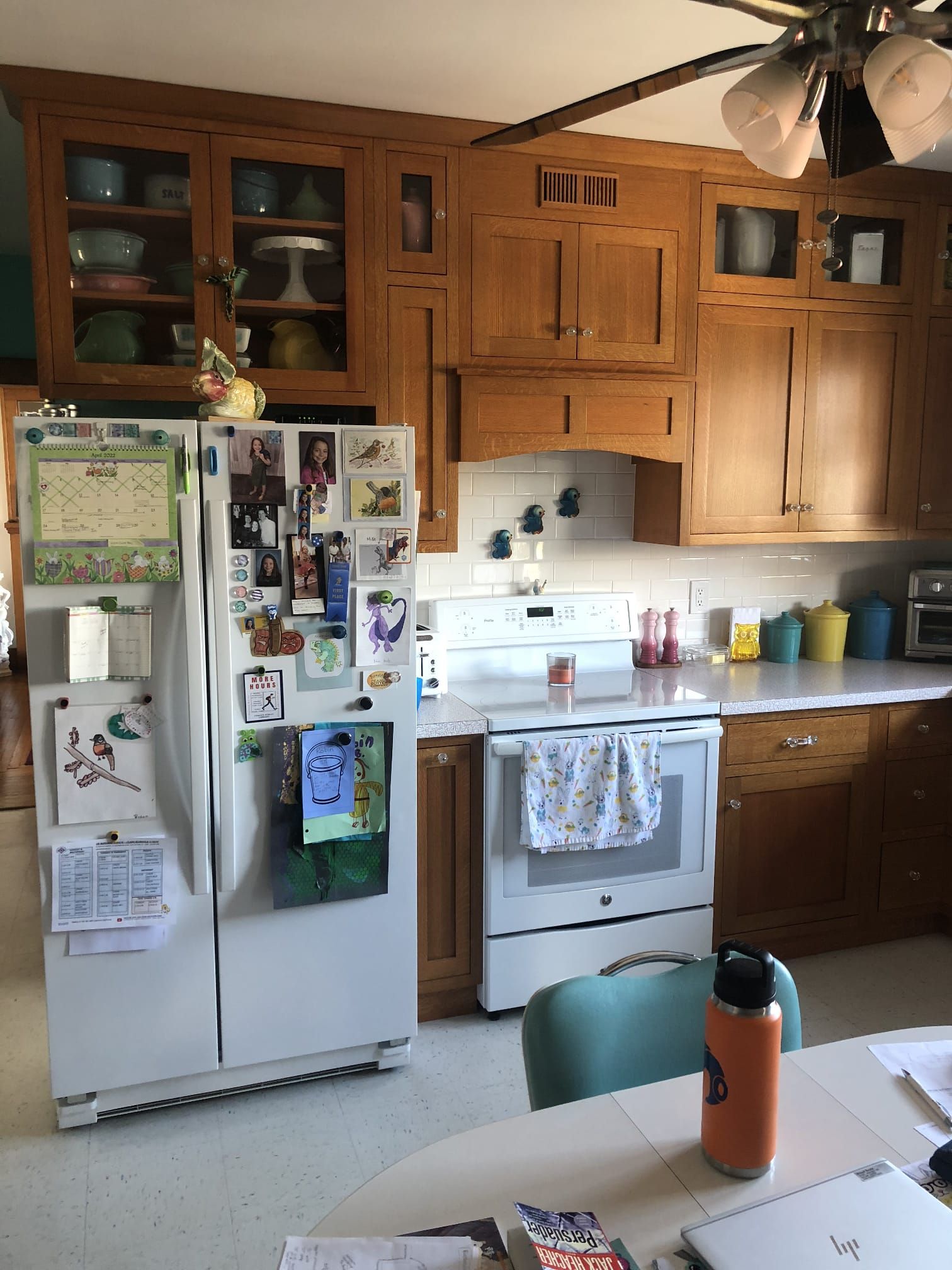Kitchen with white refrigerator covered in notes, wooden cabinets, stove, and table in foreground.