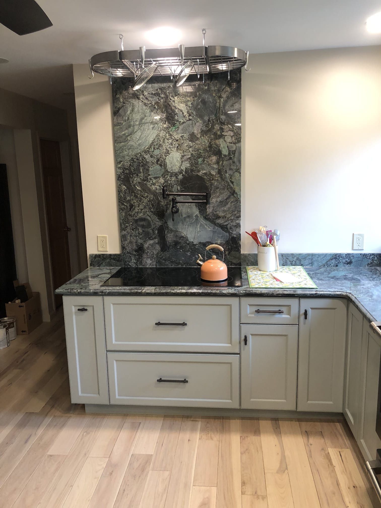 Modern kitchen island with marble countertop, pendant light, and granite backsplash, with a small orange kettle.