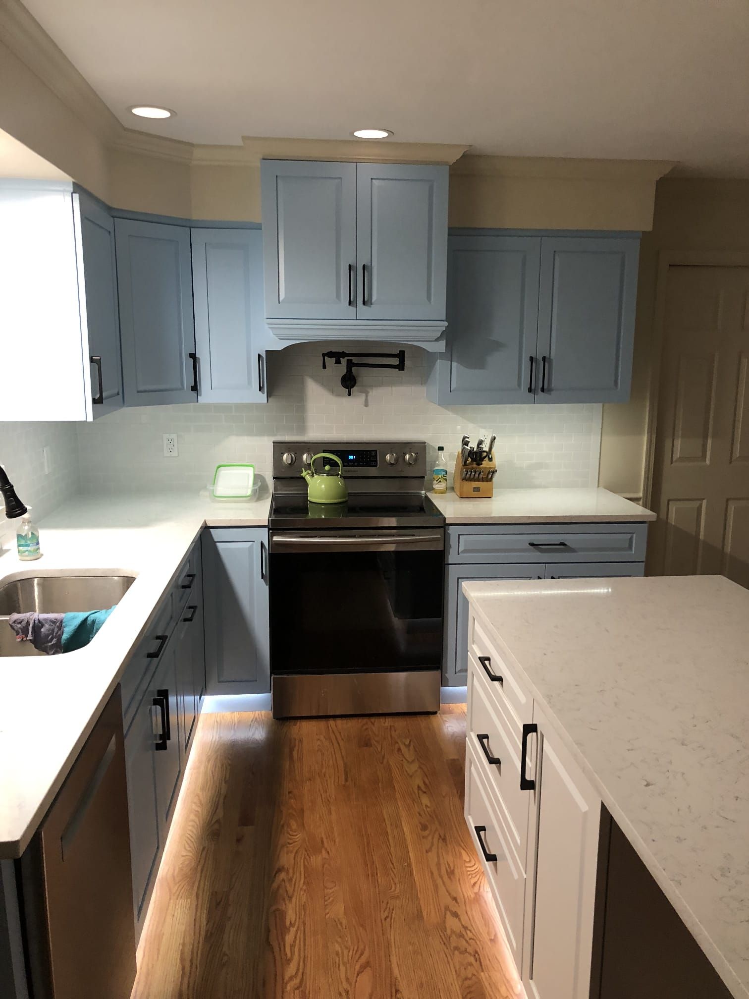 Compact kitchen with blue cabinets, black stove, white countertops, and hardwood floor.