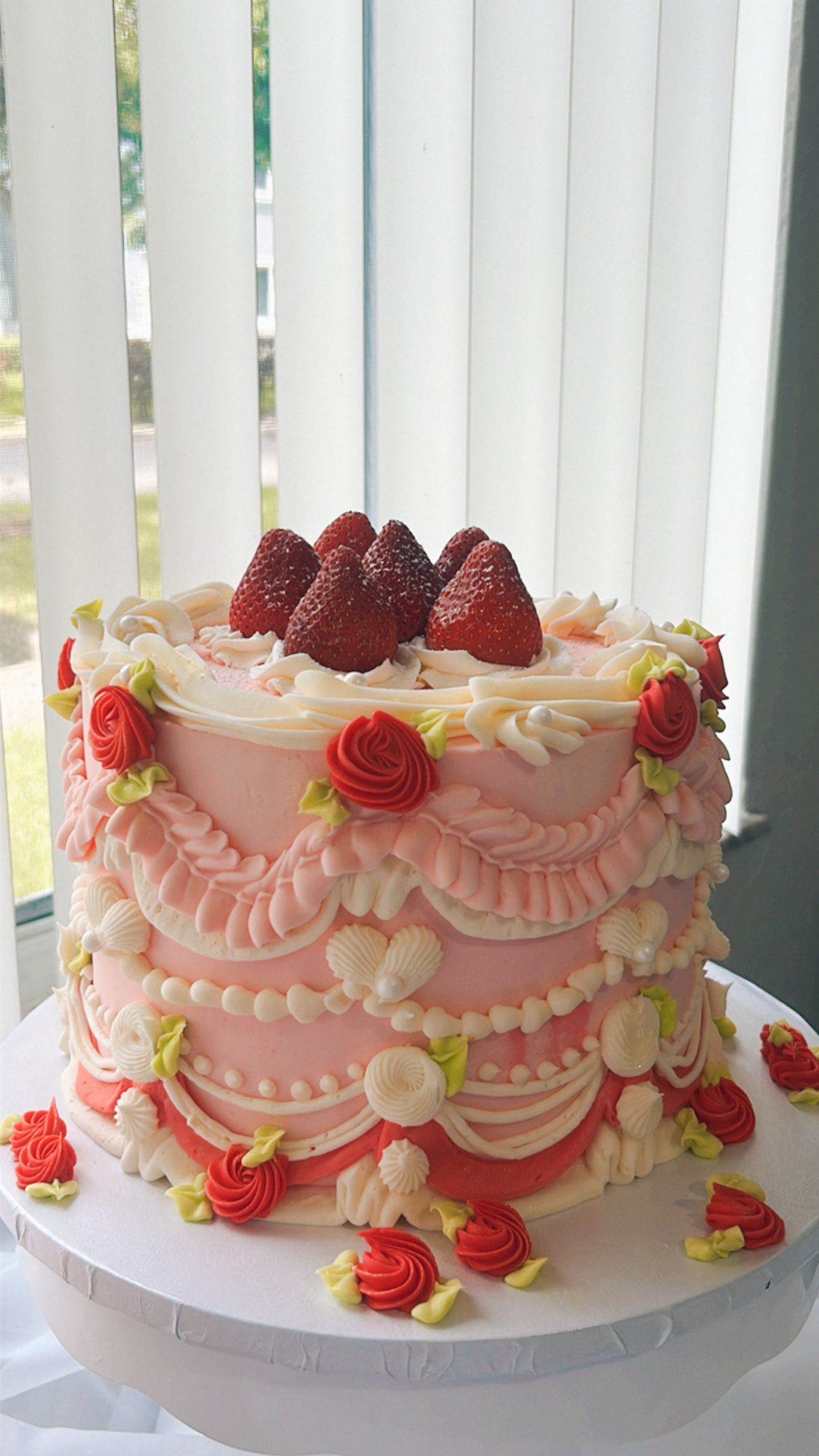 A pink cake with strawberries on top is sitting on a white plate.