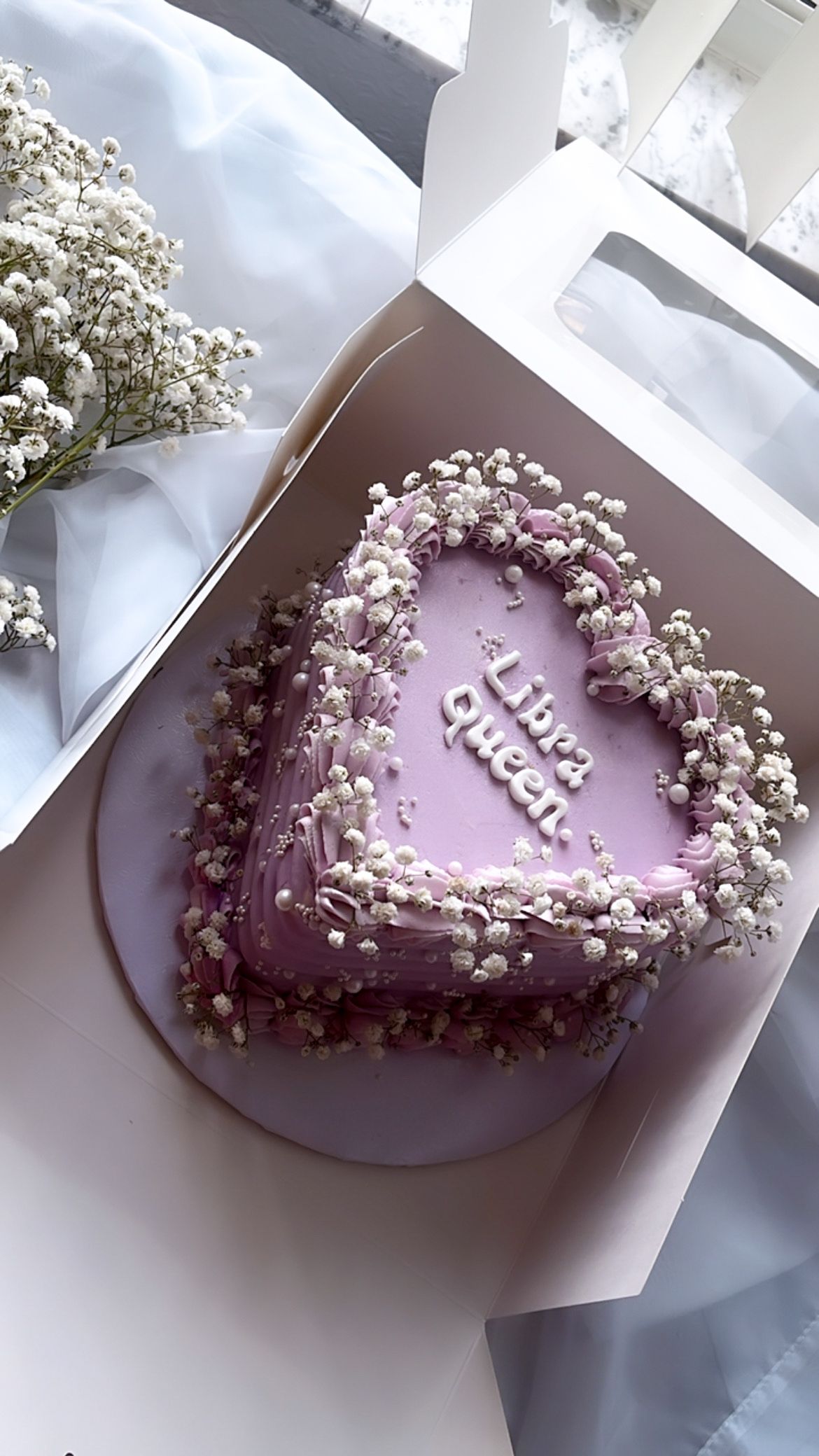 A heart shaped cake in a box with baby 's breath on it.