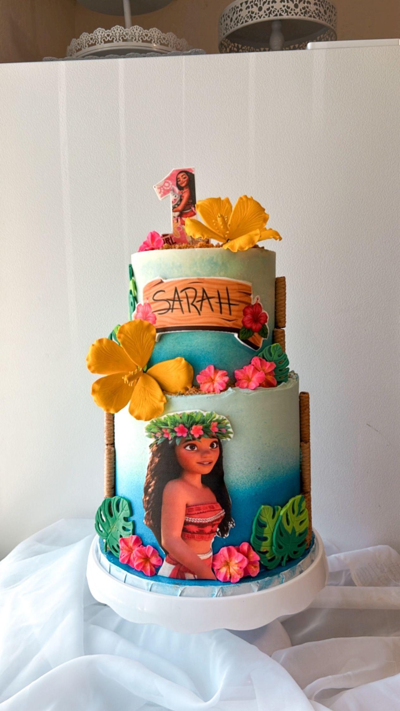 A three tiered cake with a picture of moana on it is sitting on a table.