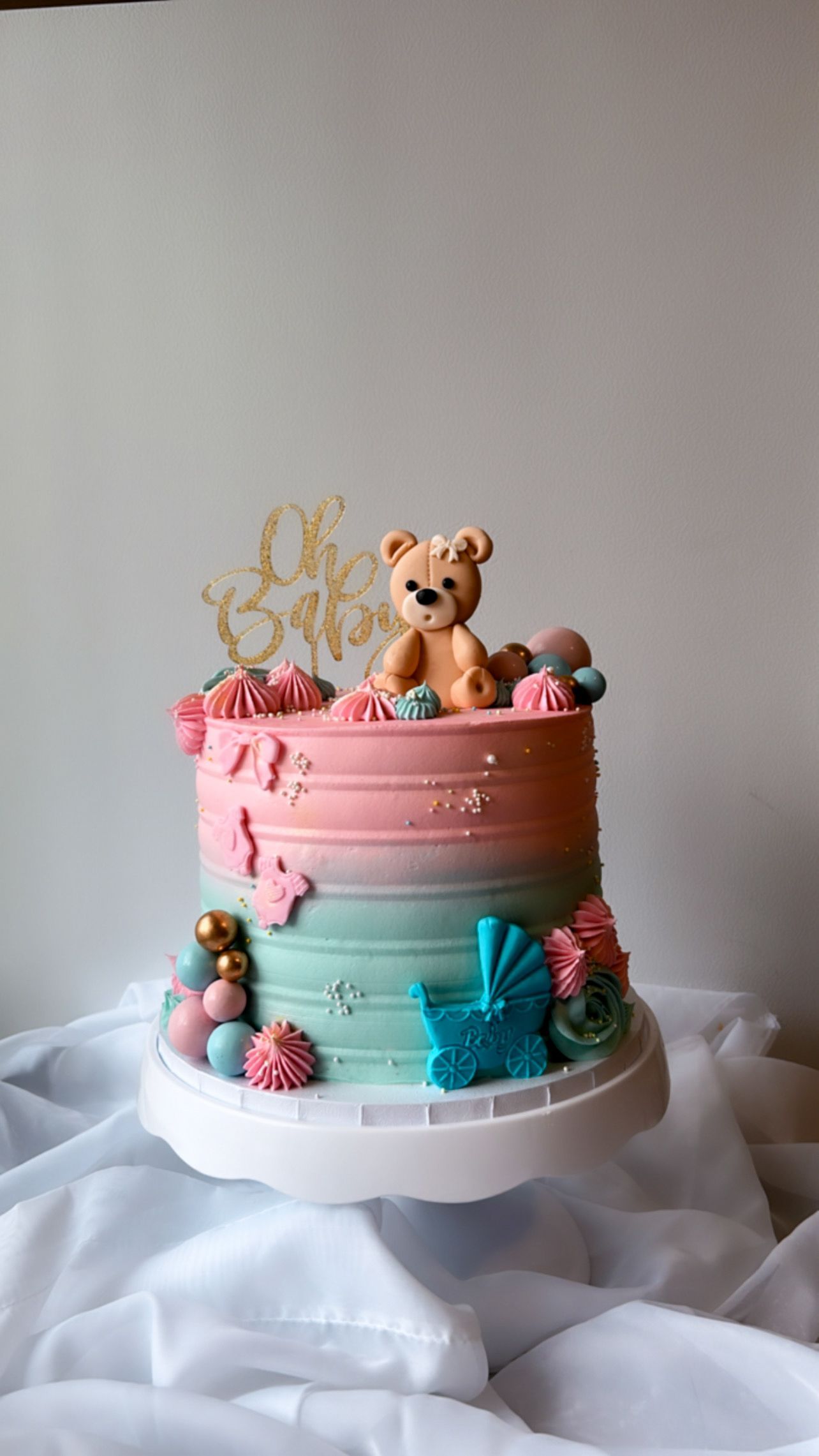 A pink and blue cake with a teddy bear on top of it.